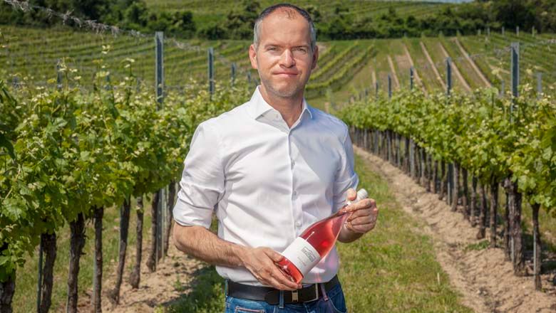 Muž na vinici s lahví růžového vína.