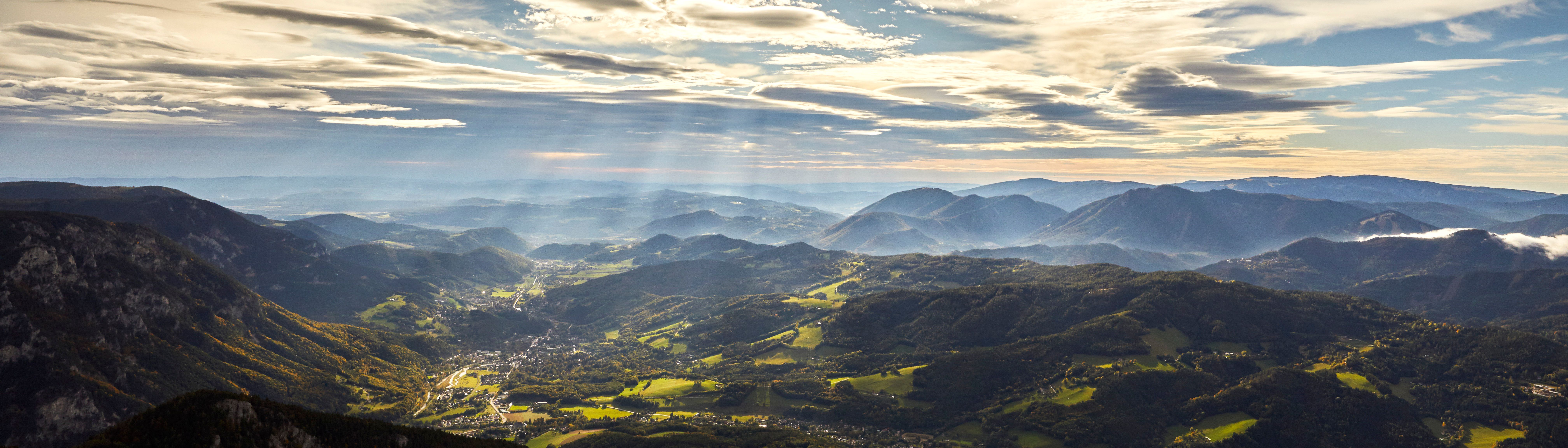 Panoramatický pohled na Raxské Alpy se slunečními paprsky a mraky na obloze.