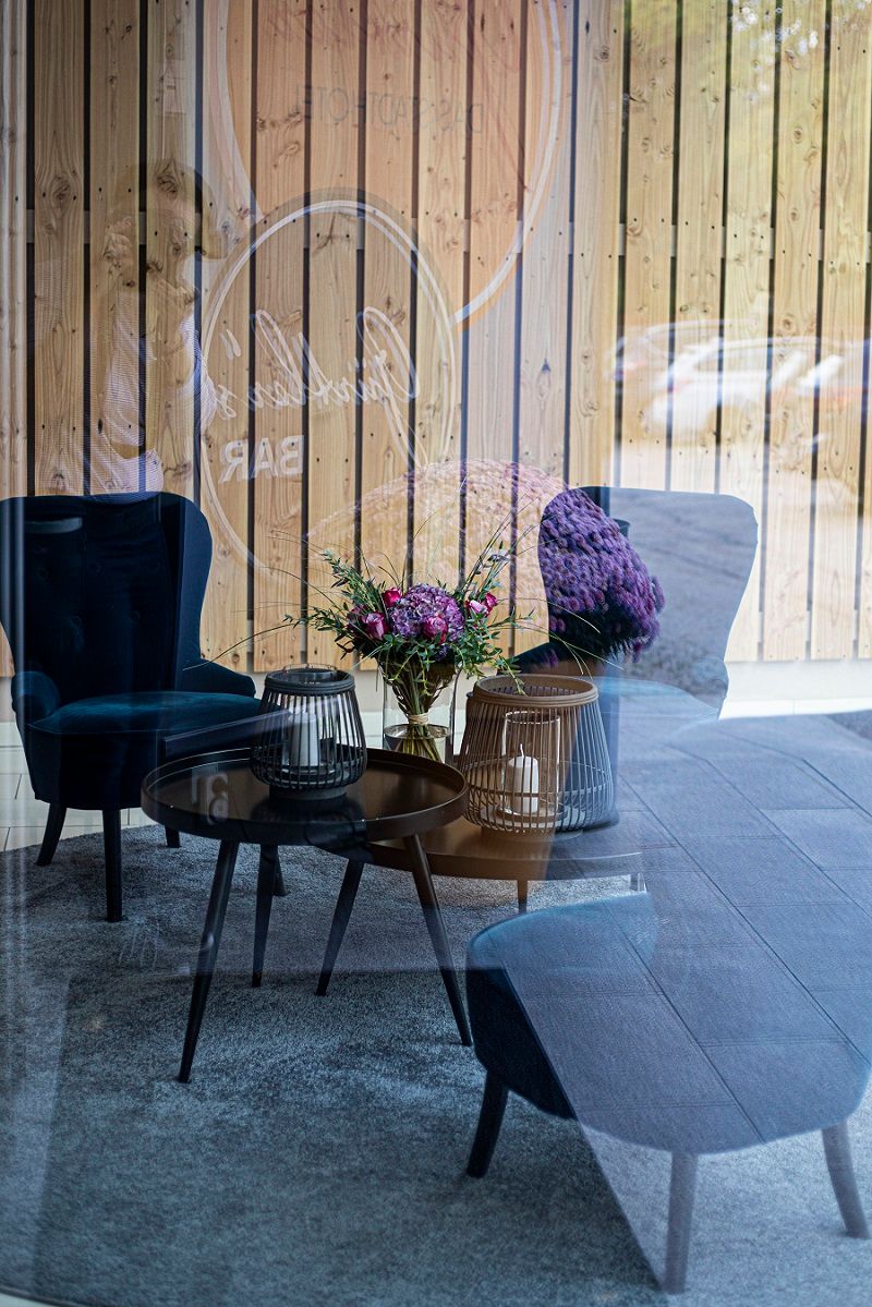 Útulný salonek s modrými křesly, stolem se svíčkami a kyticí květin, která se odráží ve skleněné stěně.