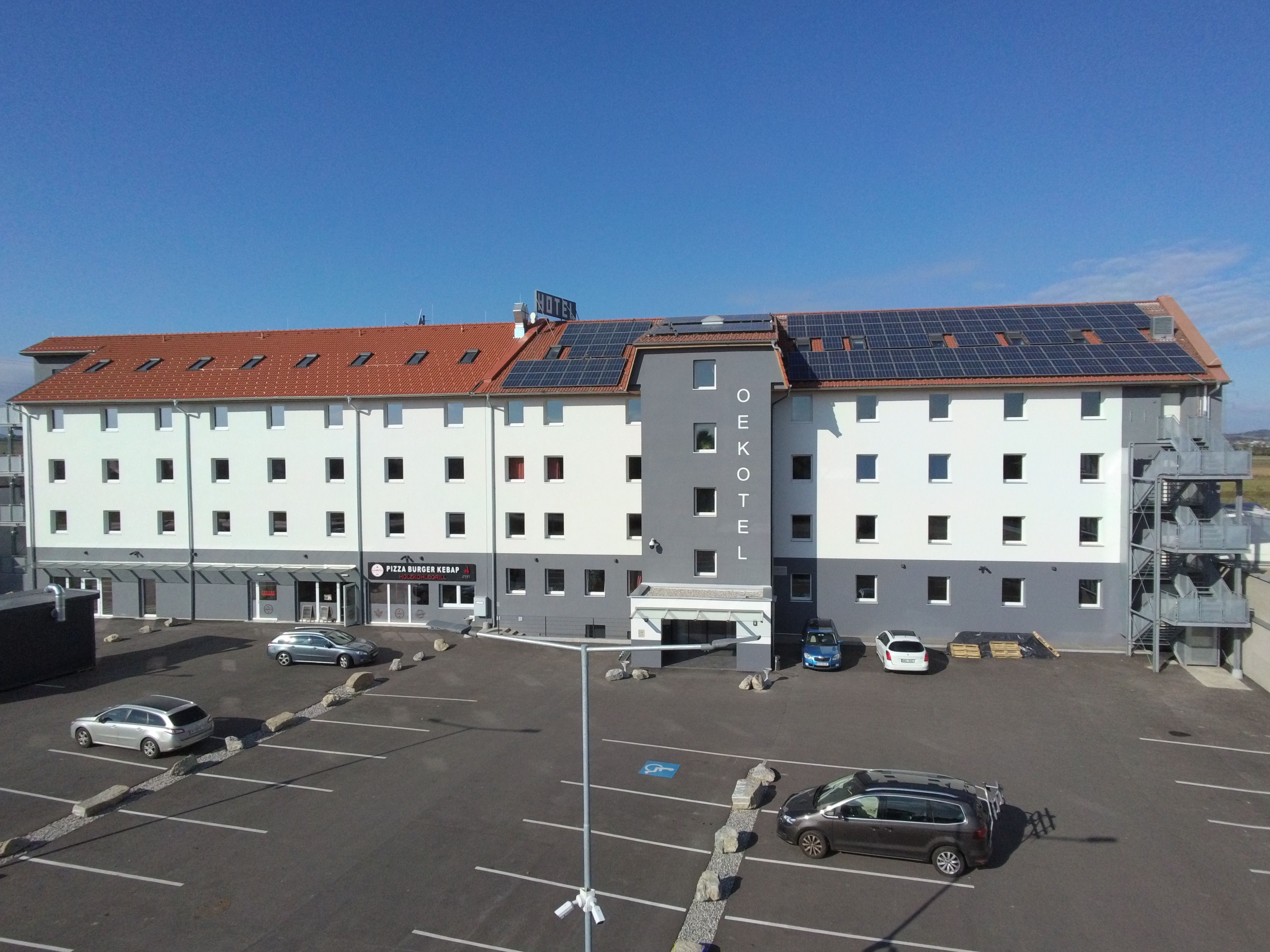 OEKOTEL Föhrenhain se solárními panely na střeše a parkovištěm před budovou.