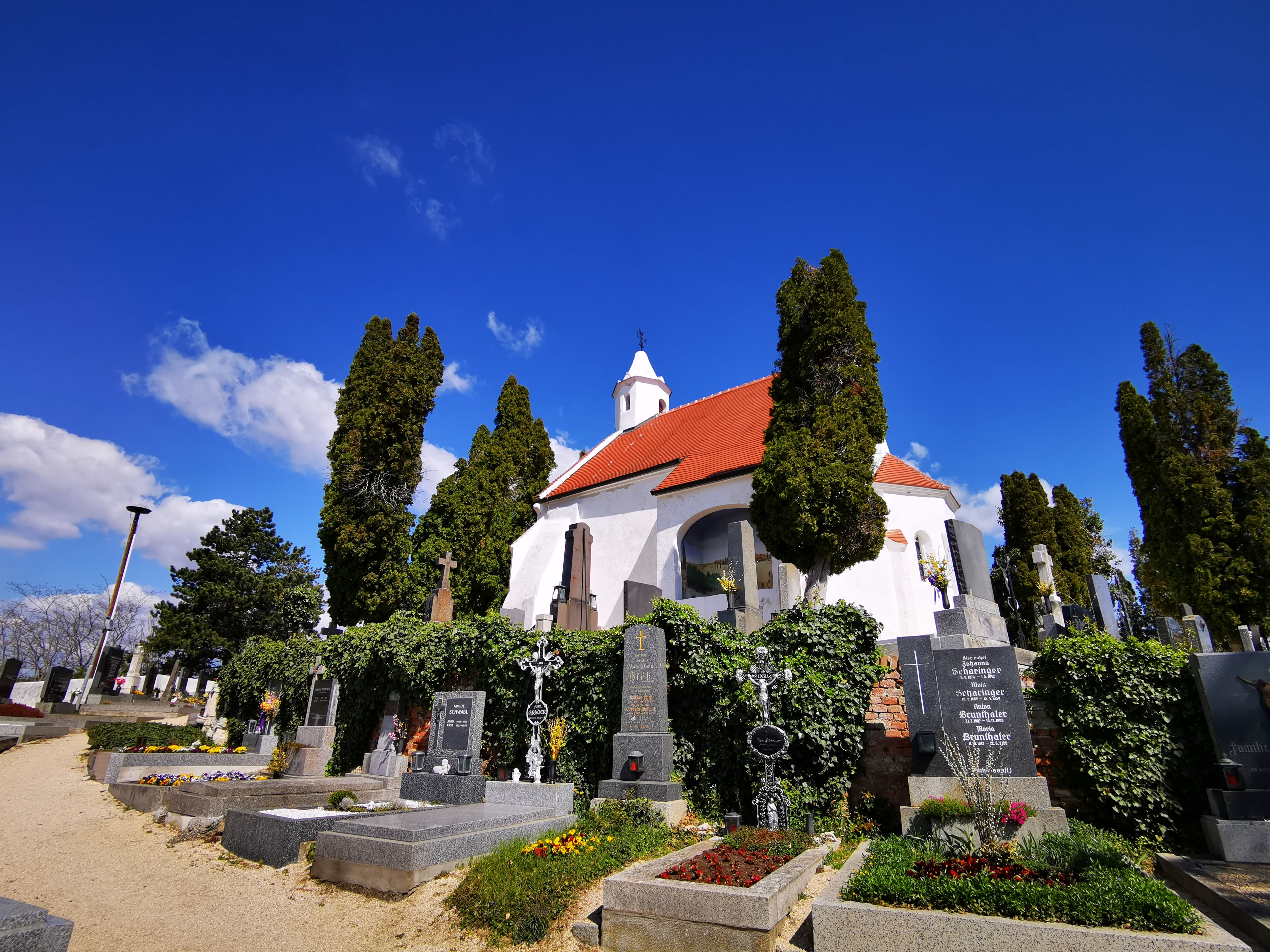 Kostel Kunigungenkirche v Mailbergu se hřbitovem a kvetoucími hroby v popředí.