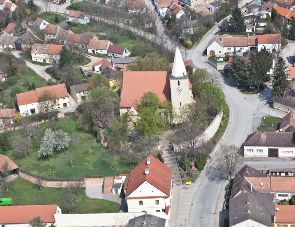Letecký pohled na kostel ve vesnici s okolními domy a ulicemi.