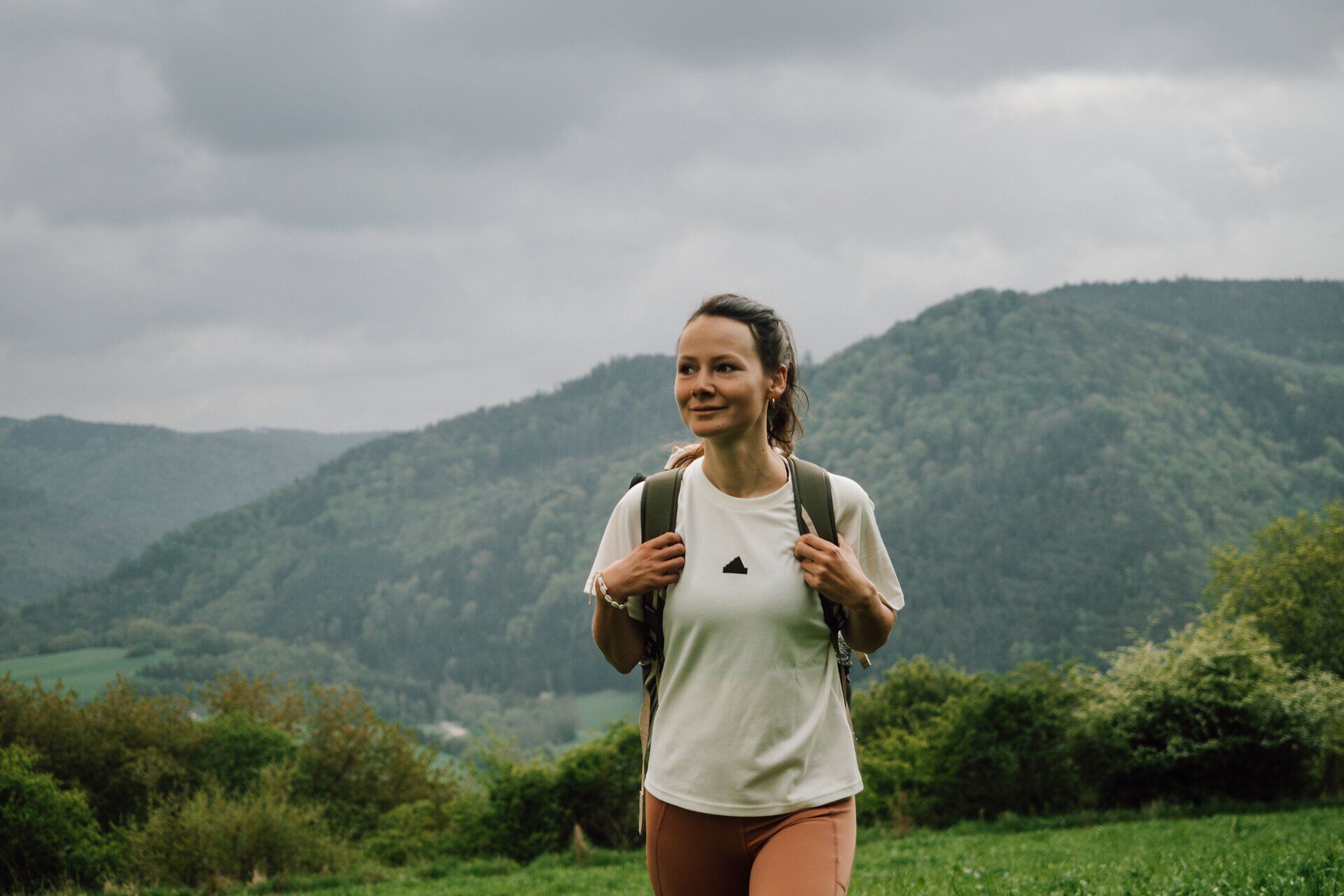 Turista si užívá čerstvý horský vzduch a úchvatný výhled na kopce a husté lesy. Mraky na obloze dodávají scenérii mystickou atmosféru, zatímco příroda je v plném rozkvětu. Toto idylické prostředí vybízí k odpočinku a poznávání krás okolí.