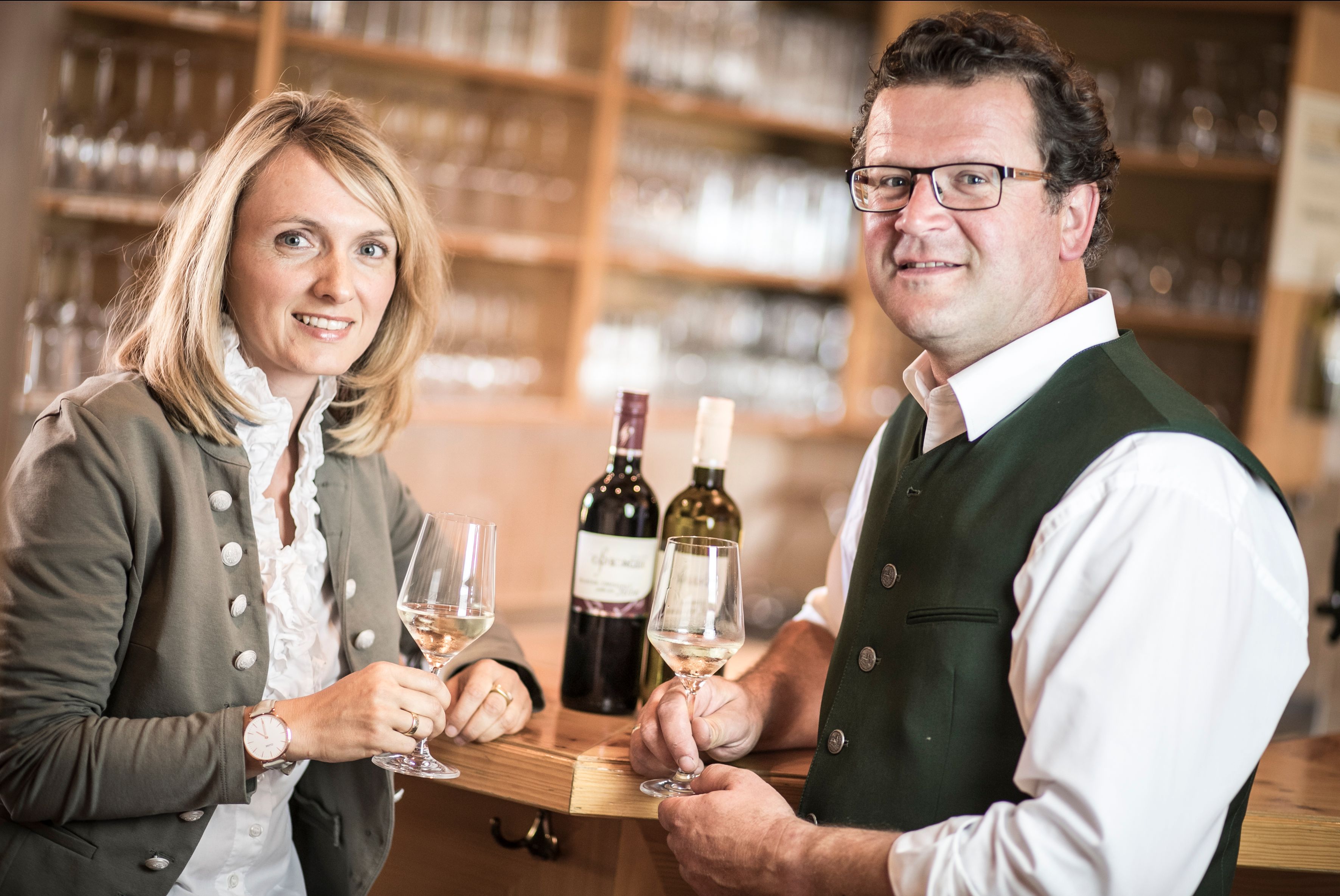 Dvě osoby v tradičním oděvu držící skleničky na víno ve vinárně.