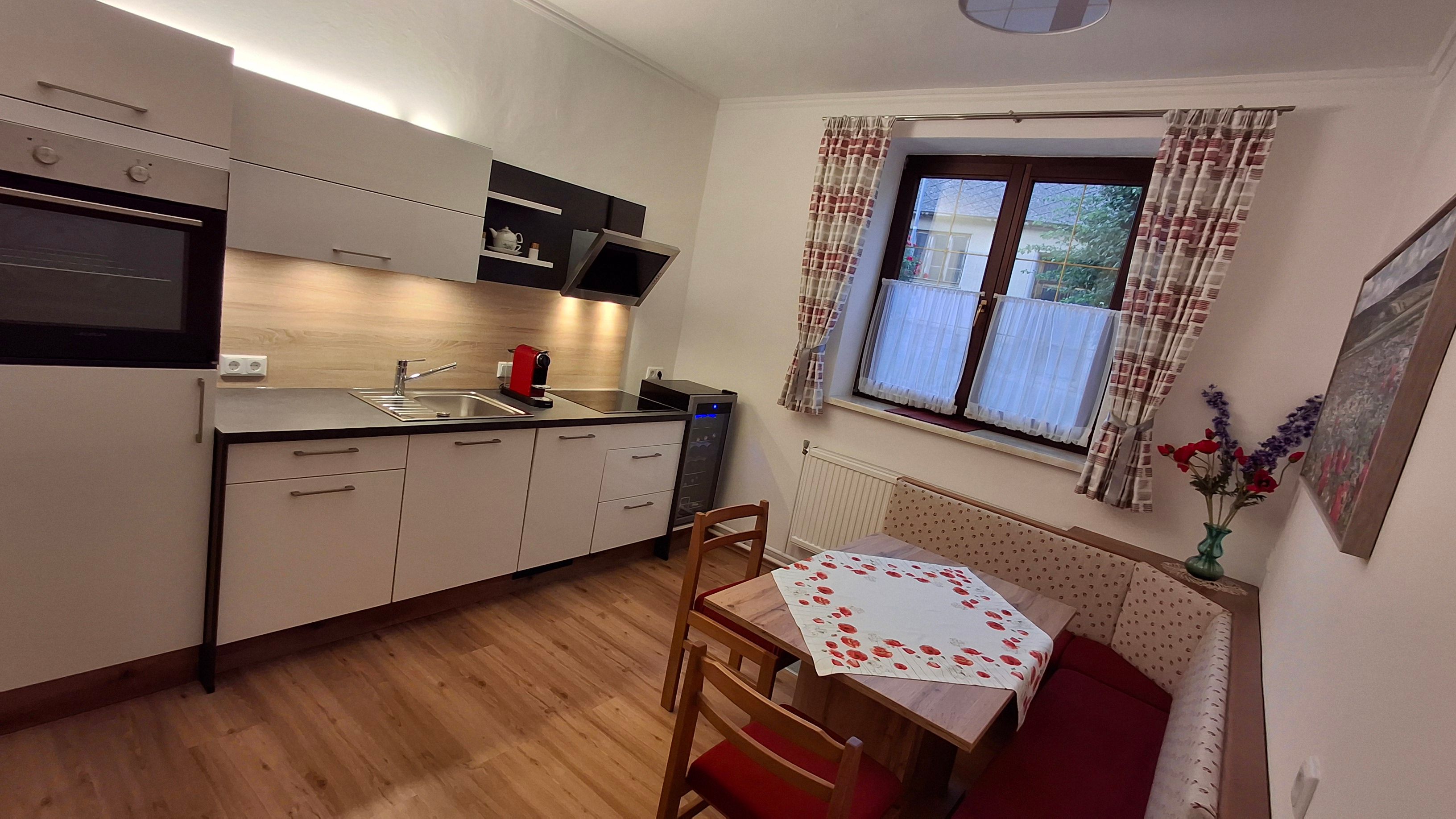 Moderní kuchyně s rohovou lavicí, stolem a oknem se závěsy.