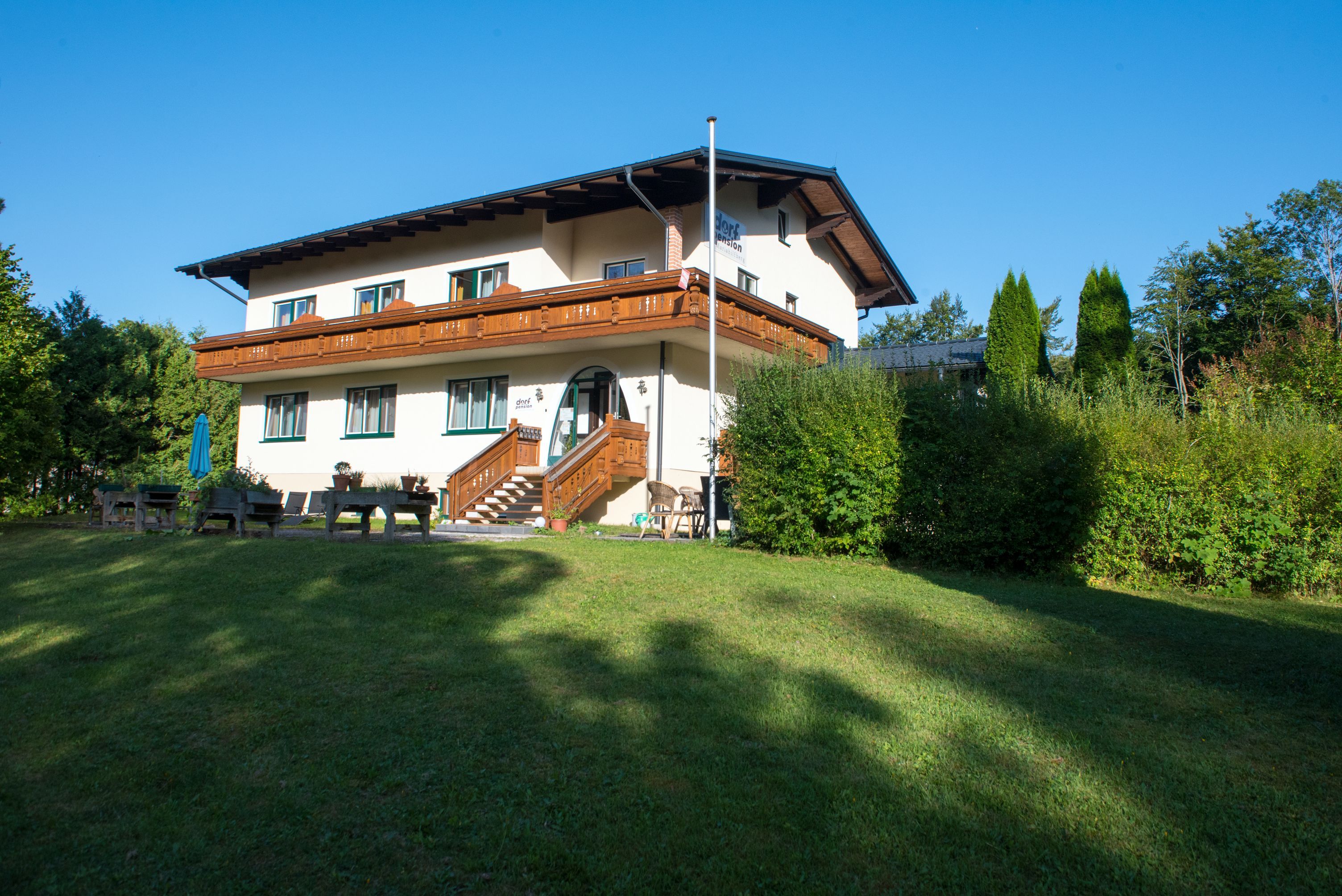 Dvoupodlažní dům s dřevěnou verandou a zahradou.