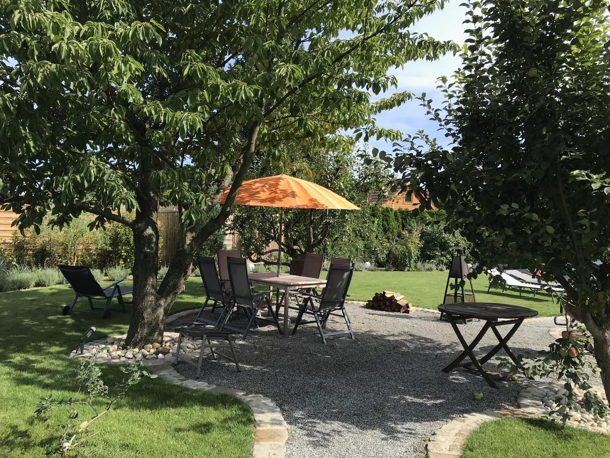 Zahrada s posezením pod stromy, stůl a židle, oranžový slunečník.
