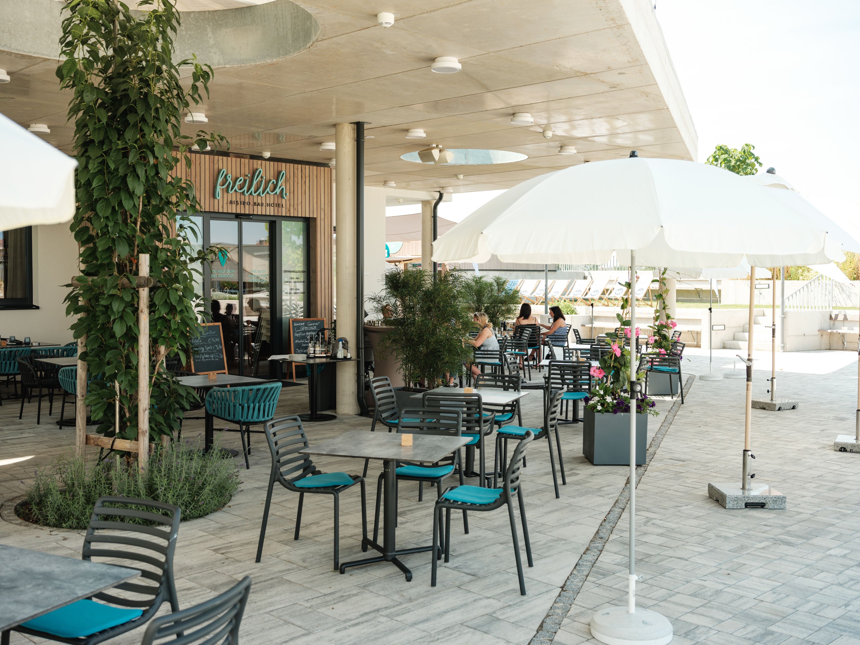 Venkovní prostor kavárny se stoly, židlemi a slunečníky.