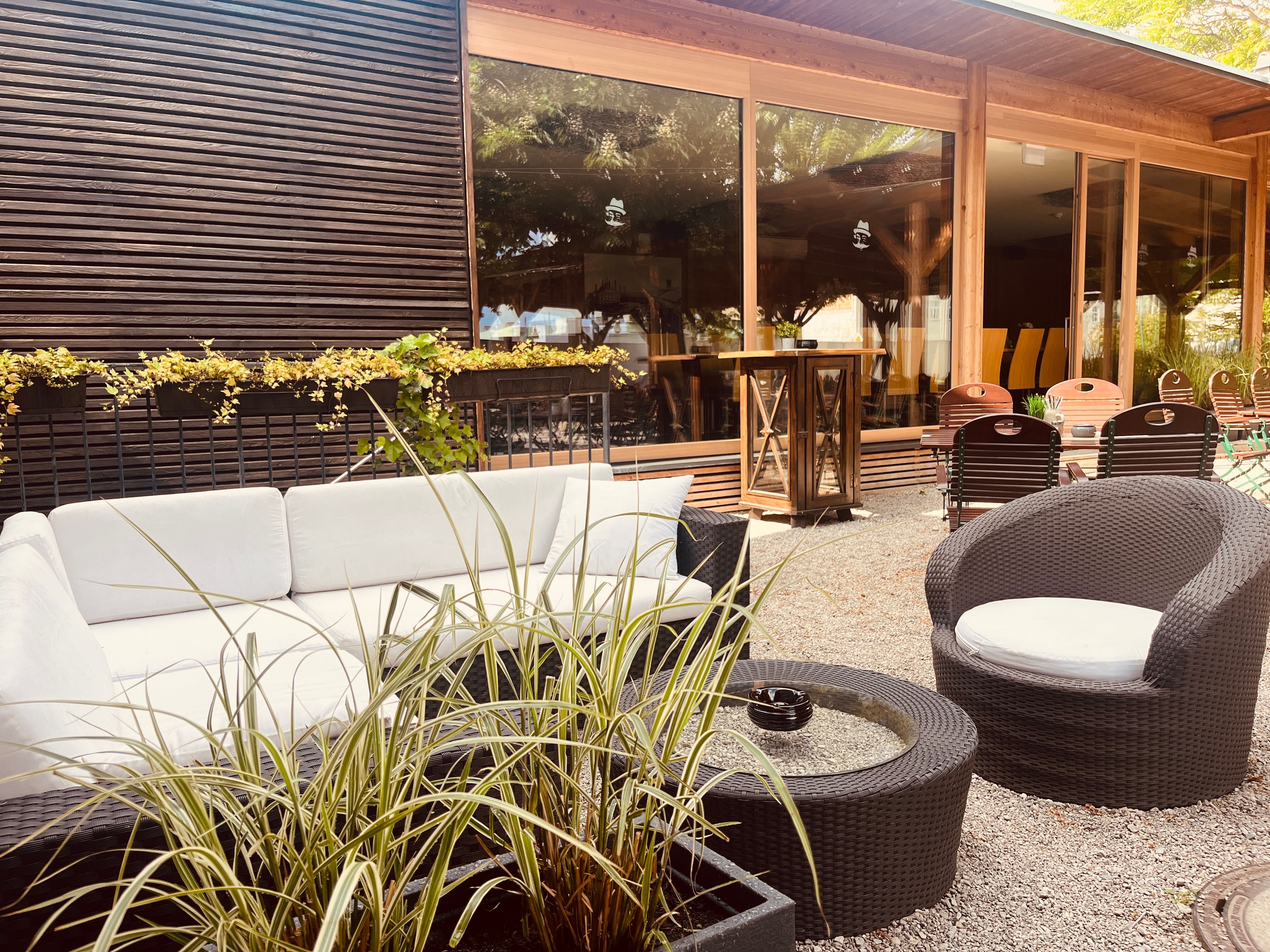 Útulný venkovní salonek s bílými pohovkami, kulatými stoly a rostlinami.