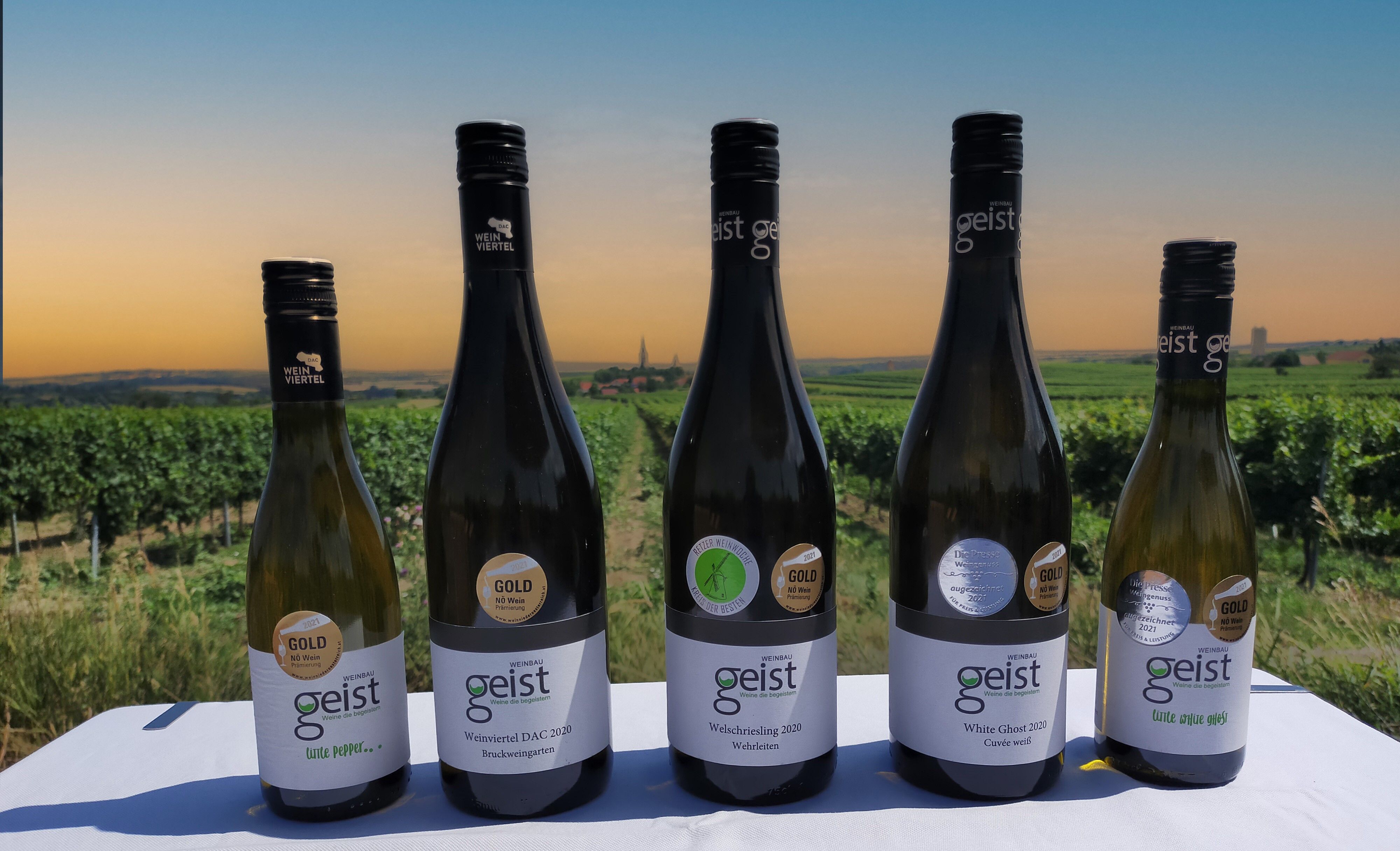 Šest lahví vína Geist před vinicí při západu slunce.