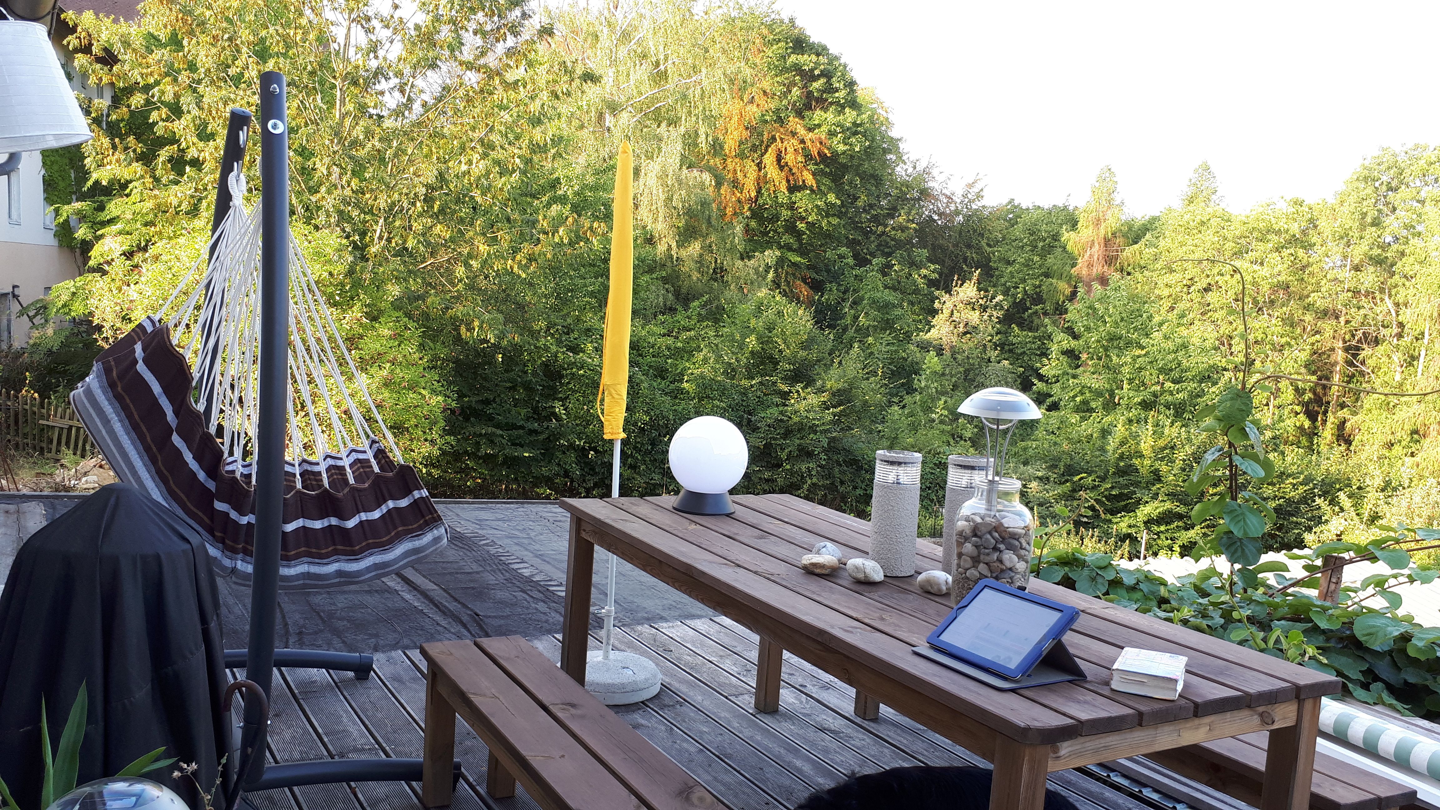 Terasa s houpací sítí, dřevěným stolem a výhledem na zelené stromy.