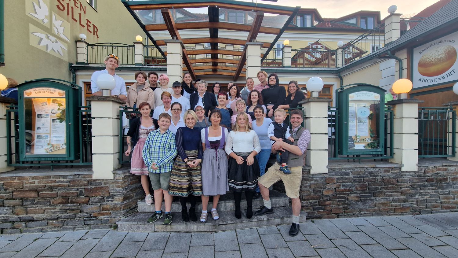 Skupina lidí stojí před budovou s nápisem Kirchenwirt.