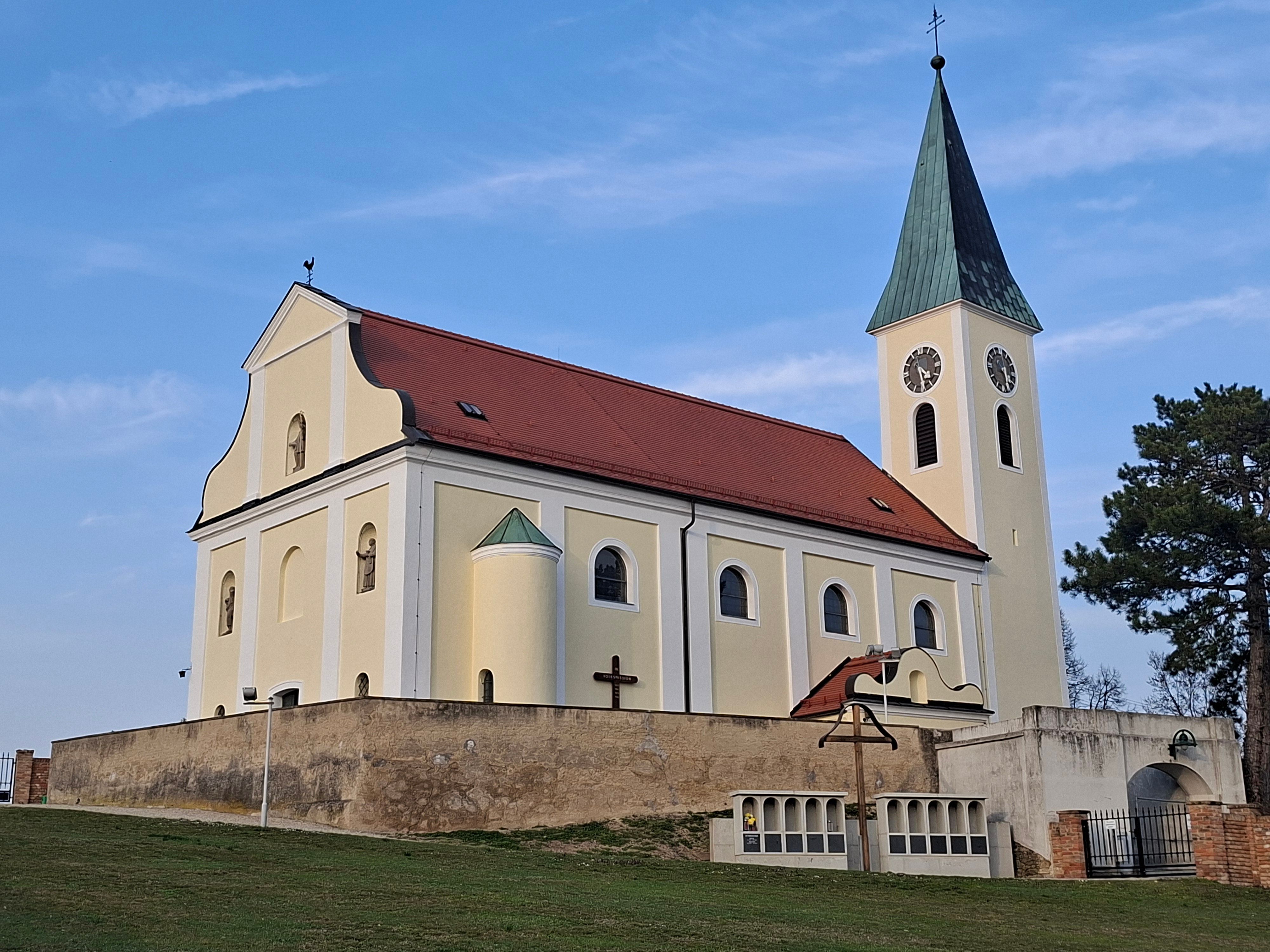 Kostel se žlutou fasádou a červenou střechou na pozadí modré oblohy.
