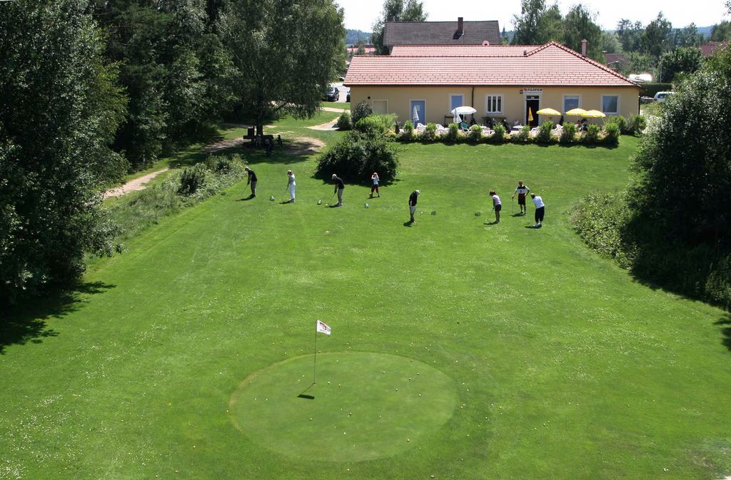 Golfové hřiště s hráči a klubovnou v pozadí.