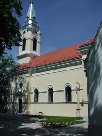Farní kostel v Tattendorfu se žlutou fasádou a červenou střechou, obklopený stromy.
