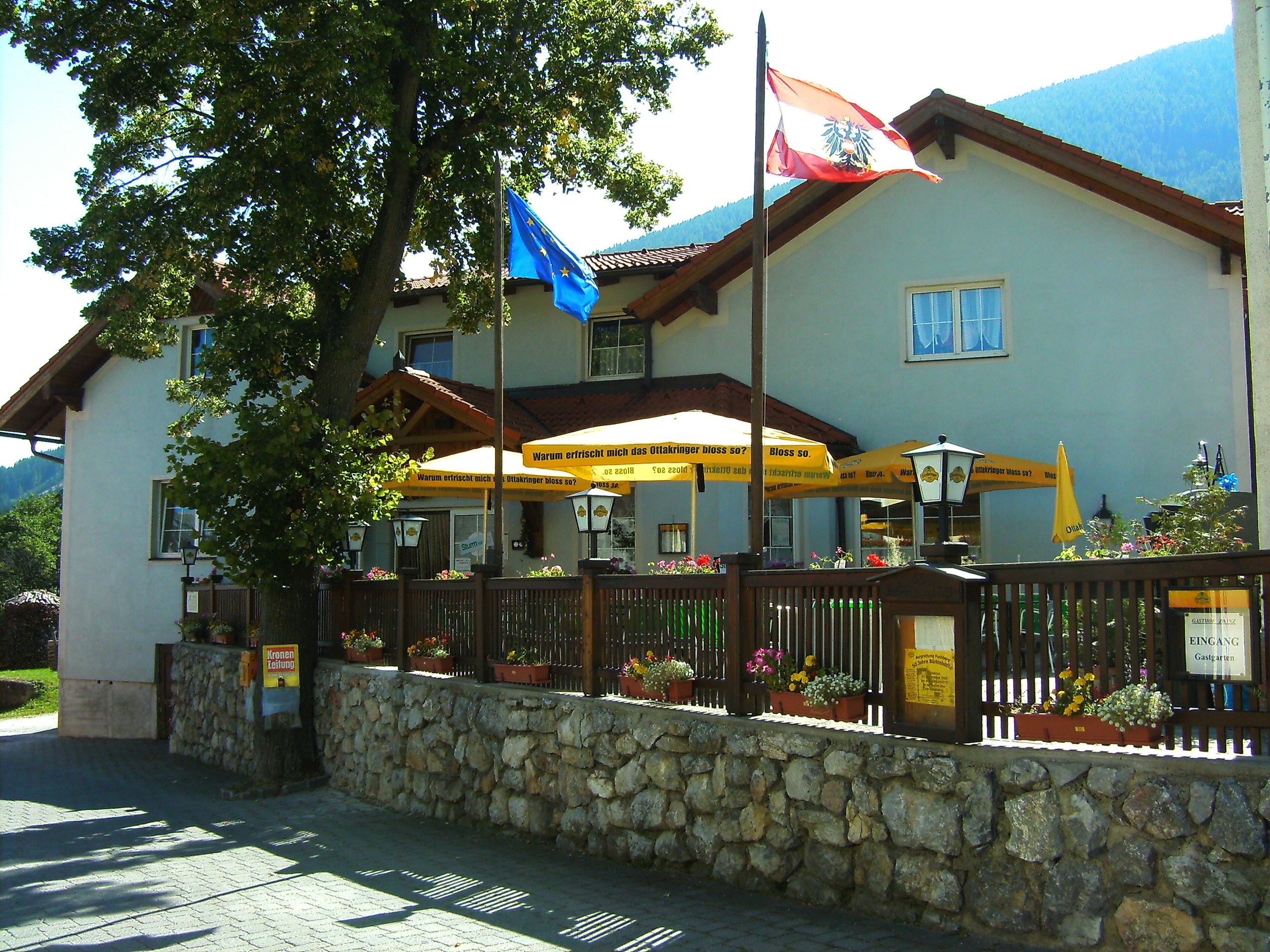 Gasthof Zwinz s terasou a slunečníky, obklopený květinami a vlajkami.