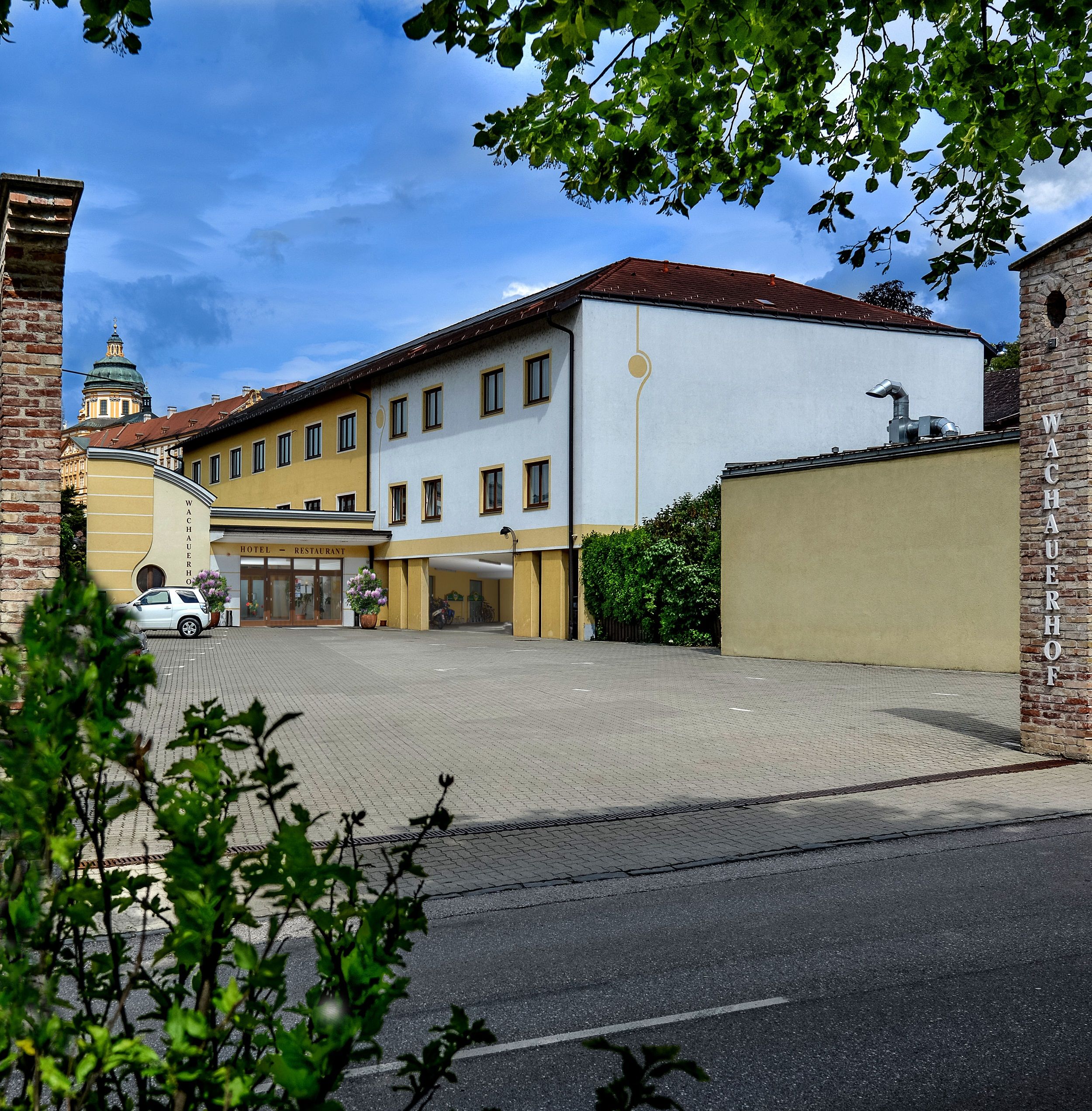 Vnější pohled na Wachauerhof v Melku s parkovištěm a fasádou budovy.