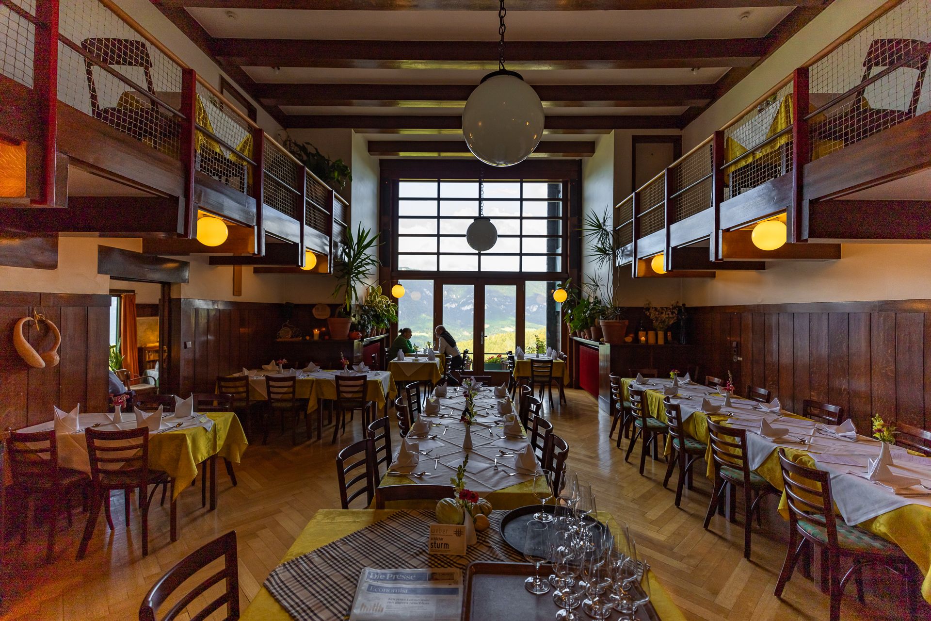 Pohled do interiéru restaurace s dřevěným nábytkem a velkými okny.