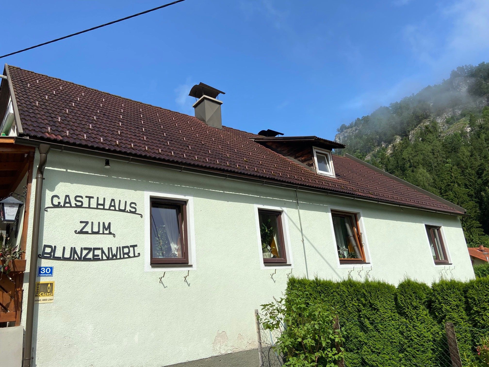 Pohled zvenčí na hostinec Zum Blunzenwirt se zeleným nátěrem a hnědou střechou.