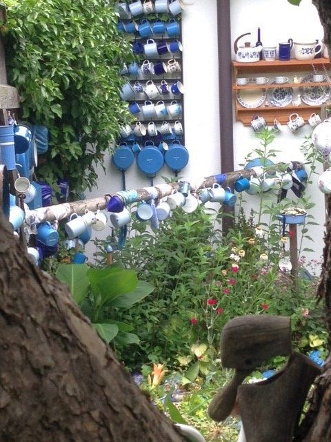 Zahrada se spoustou barevných hrníčků zavěšených na stěnách a sloupech.