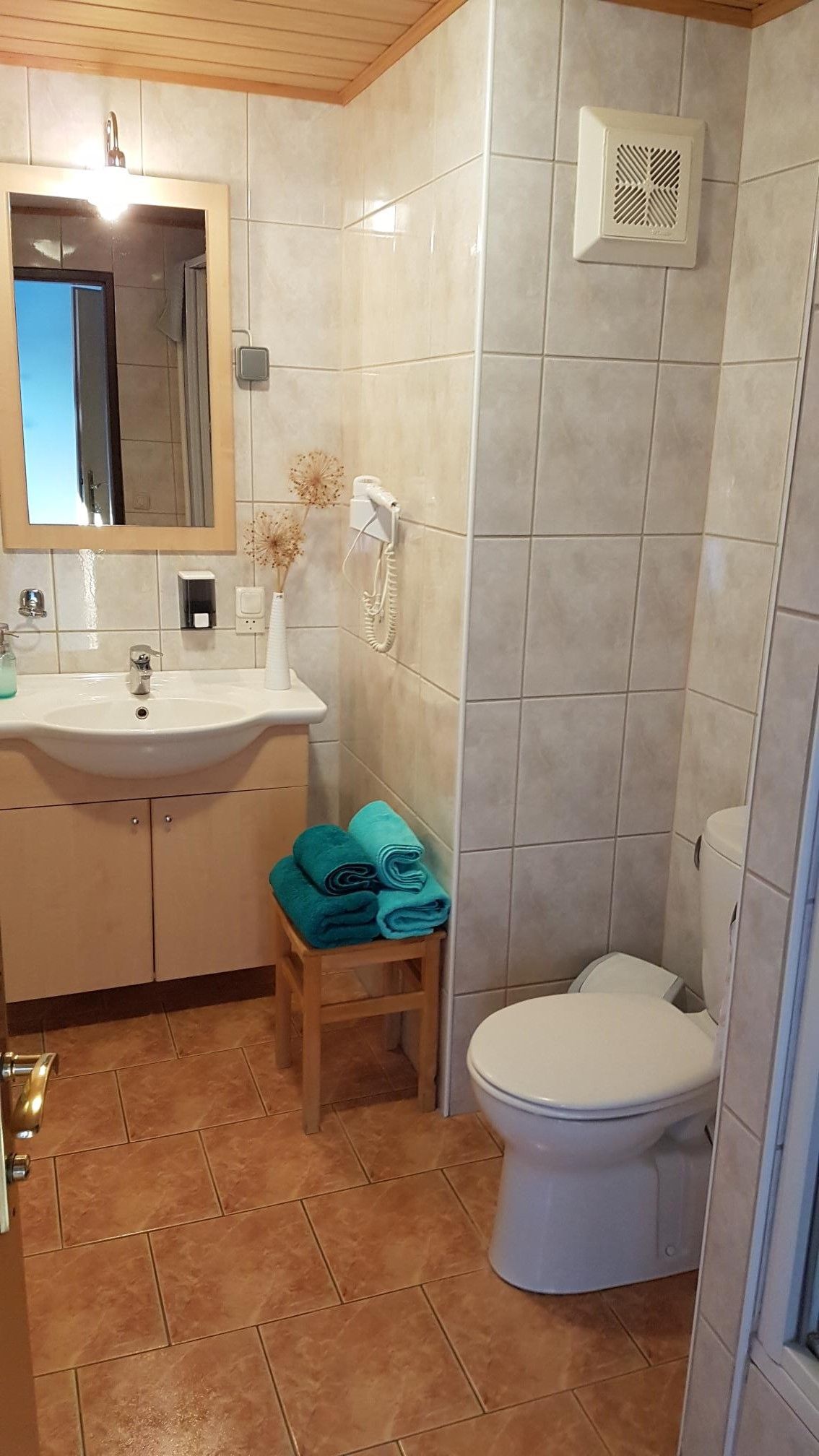 Koupelna s umyvadlem, zrcadlem, toaletou a ručníky na stoličce.