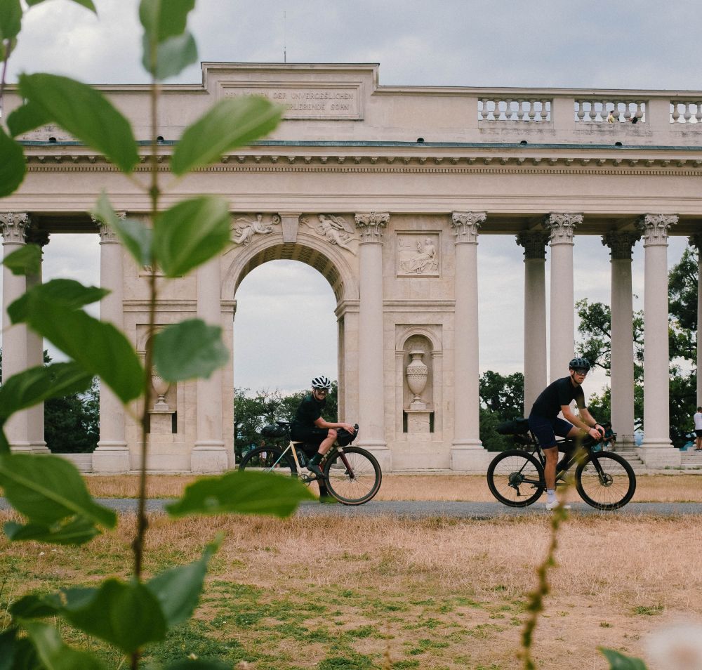 Radfahrer gleiten entspannt entlang der malerischen Landschaft, umgeben von üppigem Grün und historischen Säulen. Die sanfte Brise und die beeindruckenden Ausblicke laden dazu ein, die Schönheit der Natur in vollen Zügen zu genießen.