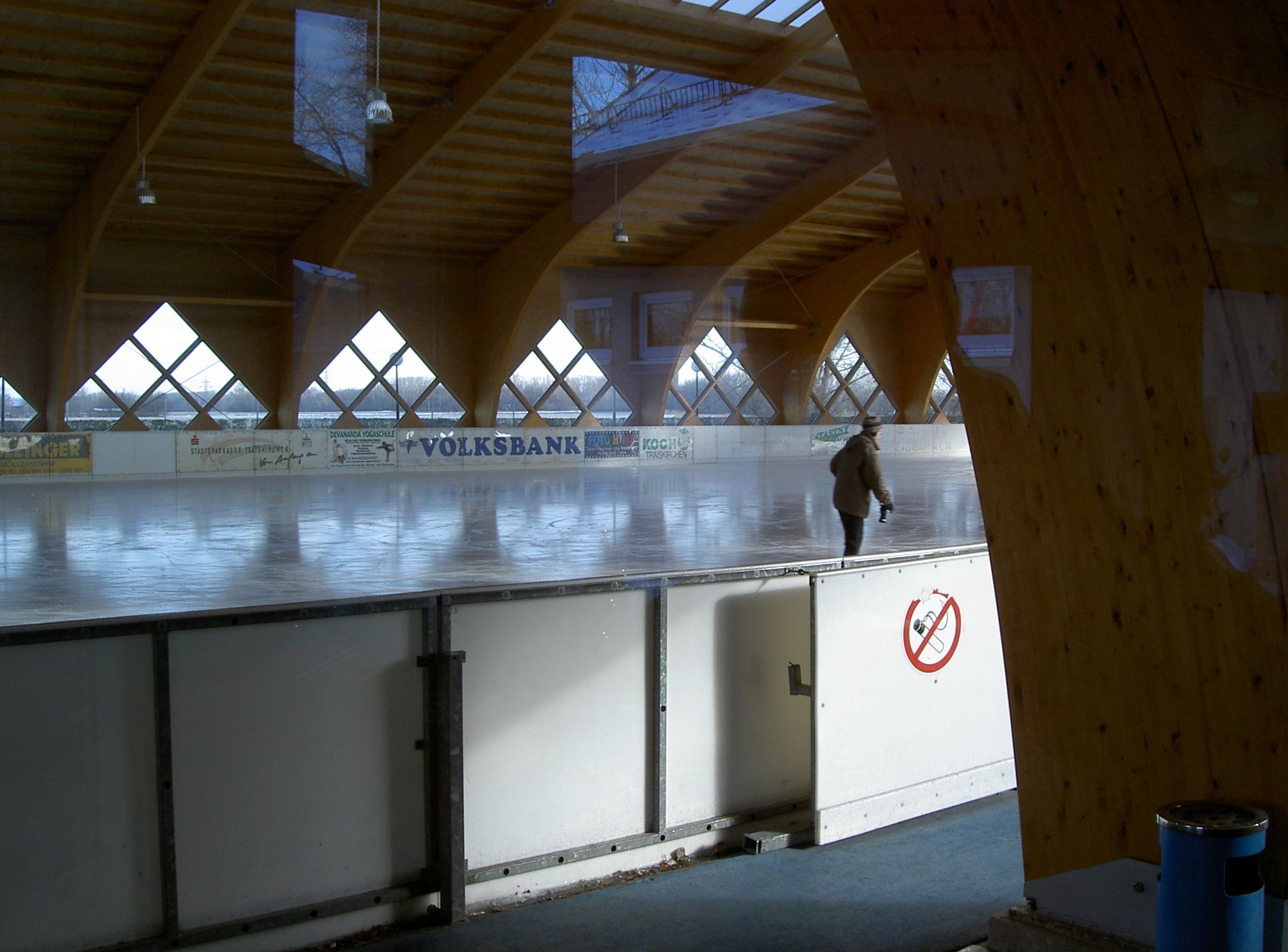 Kryté umělé kluziště, na kterém bruslí člověk. Kluziště je obklopeno dřevěnými trámy a okny.