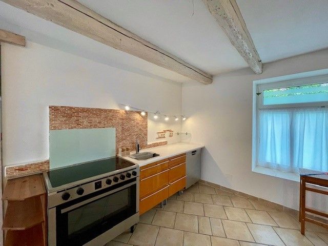 Moderní kuchyně se sporákem, dřevěnými skříňkami a dlážděnou podlahou.