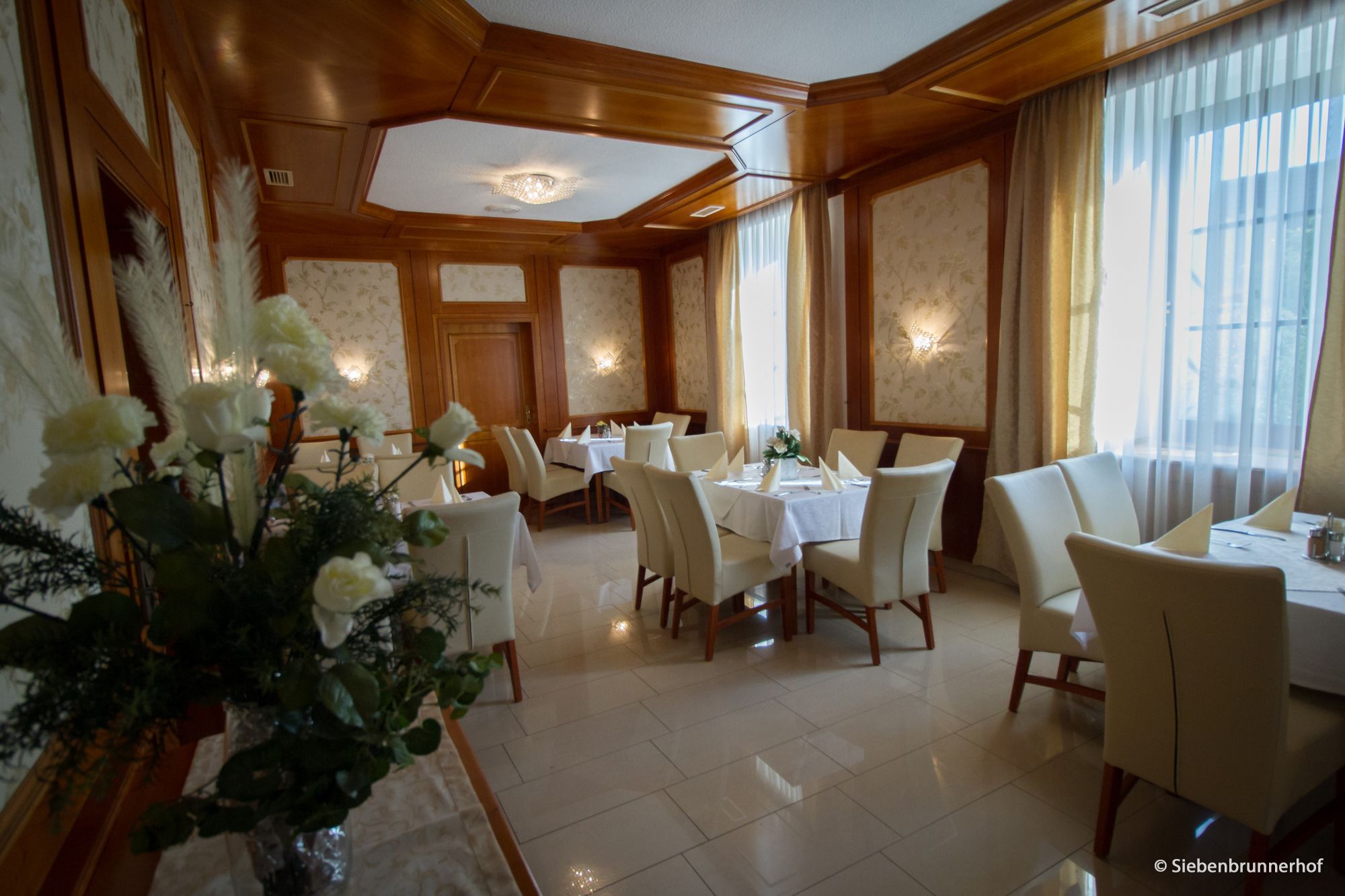 Elegantní jídelna s prostřenými stoly, bílými židlemi a květinovou výzdobou.