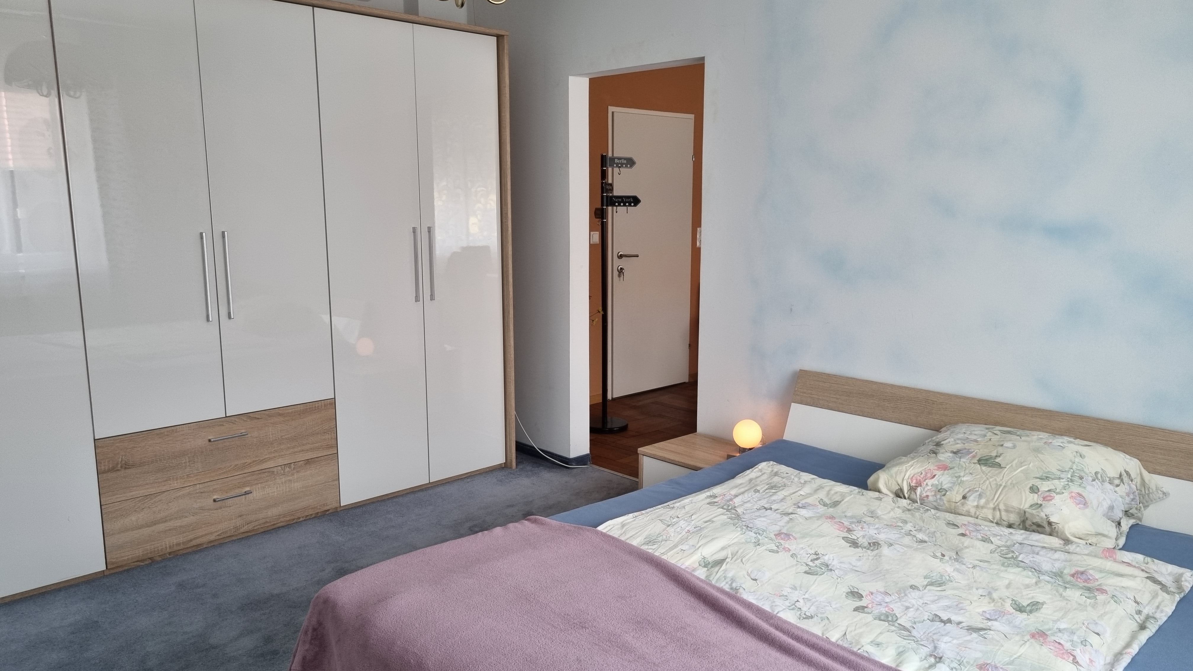 Ložnice s manželskou postelí, velkou bílou skříní a noční lampou.