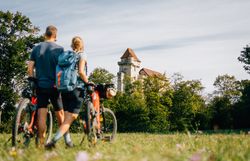 Ein Paar genießt die frische Luft und die malerische Aussicht auf die majestätische Burg Liechtenstein, während sie mit ihren Fahrrädern durch die sanften Wiesen des Wienerwaldes radeln. Die sanften Hügel und das satte Grün der Natur schaffen eine perfekte Kulisse für ein unvergessliches Abenteuer in der Natur.