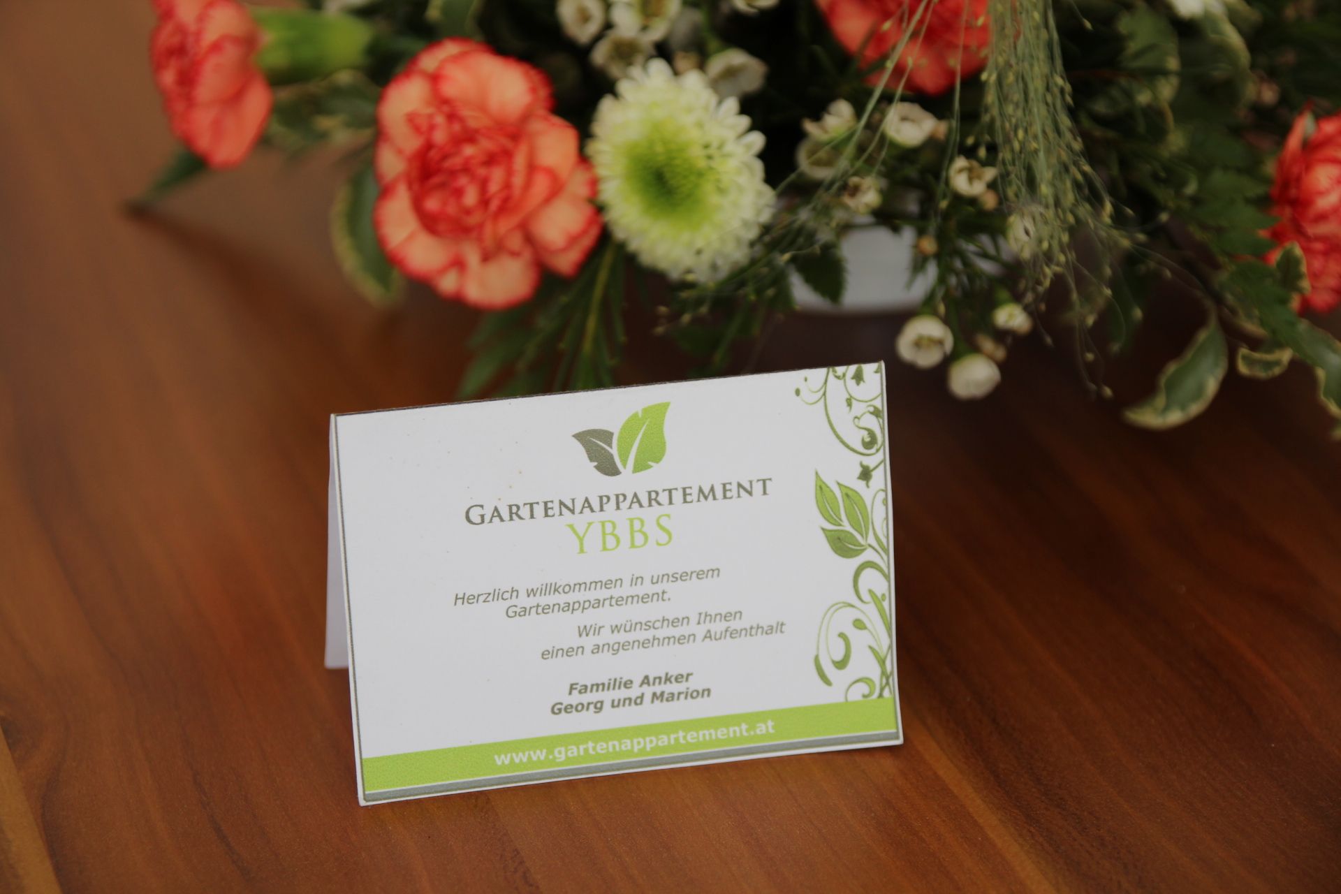 Uvítací karta Gartenappartement Ybbs na stole s květinami.