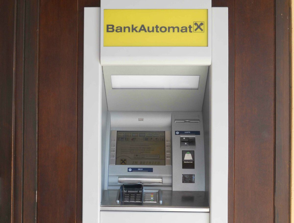 Bankomat se žlutým nápisem a logem Raiffeisen.