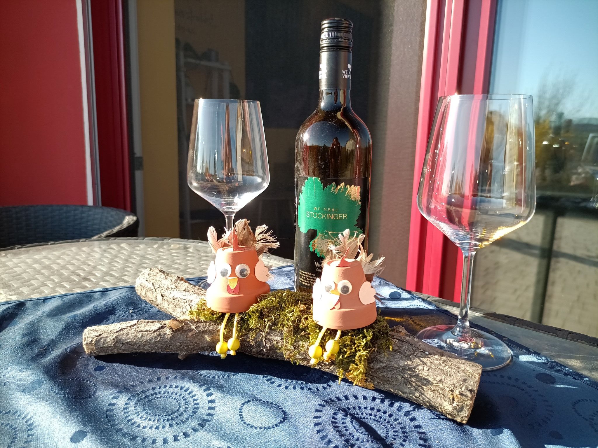 Láhev vína se dvěma prázdnými sklenicemi a dekorativními figurkami na stole.