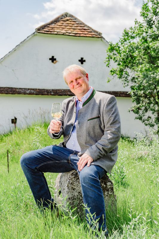 Muž sedící na kameni v přírodě a držící v ruce sklenku vína.