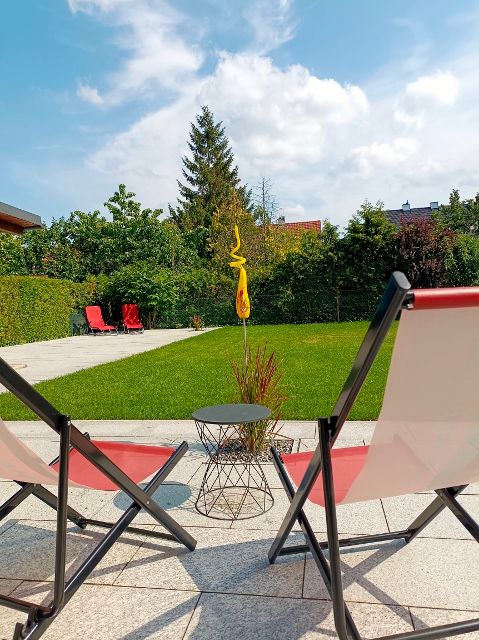 Dvě lehátka na zahradě s trávníkem a stromy v pozadí.