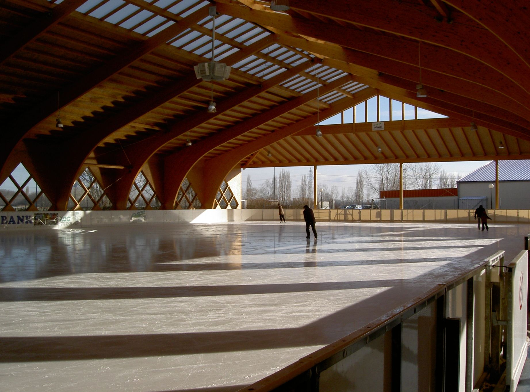 Kryté umělé kluziště s dřevěnou konstrukcí a bruslaři.