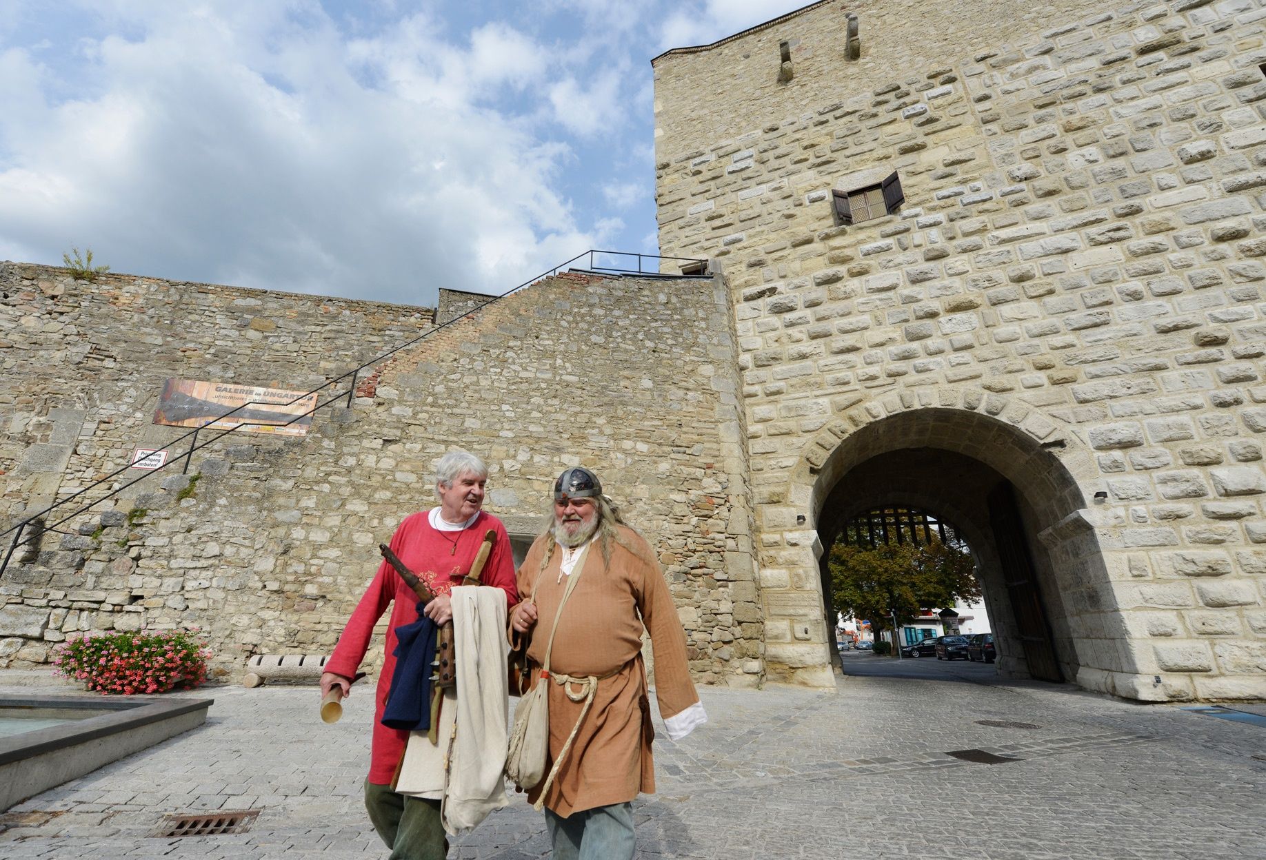 Dva muži ve středověkém oblečení před starou kamennou zdí v Hainburgu an der Donau.