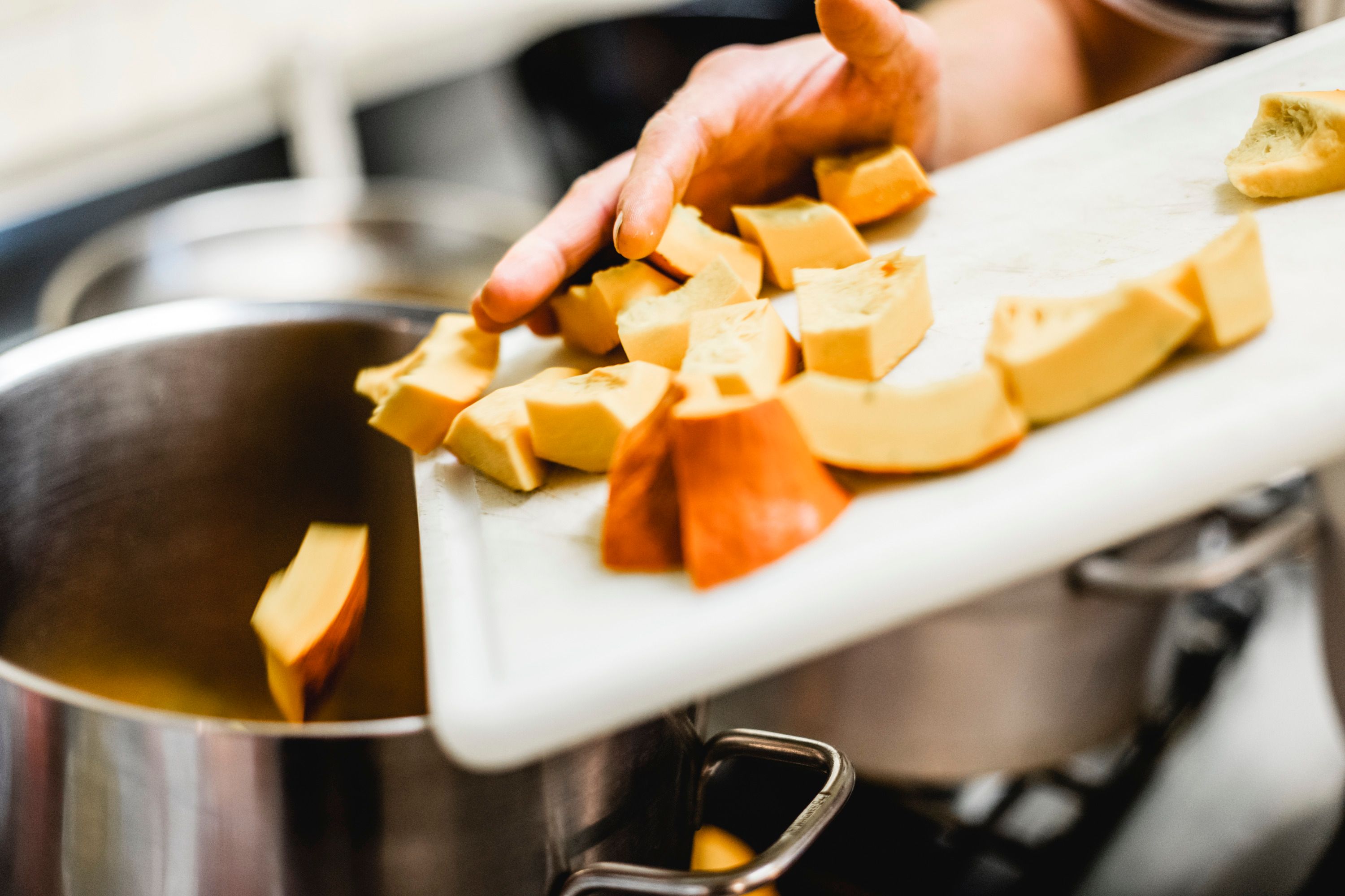 Rukou se do hrnce z prkénka na krájení tlačí nakrájené kousky dýně.