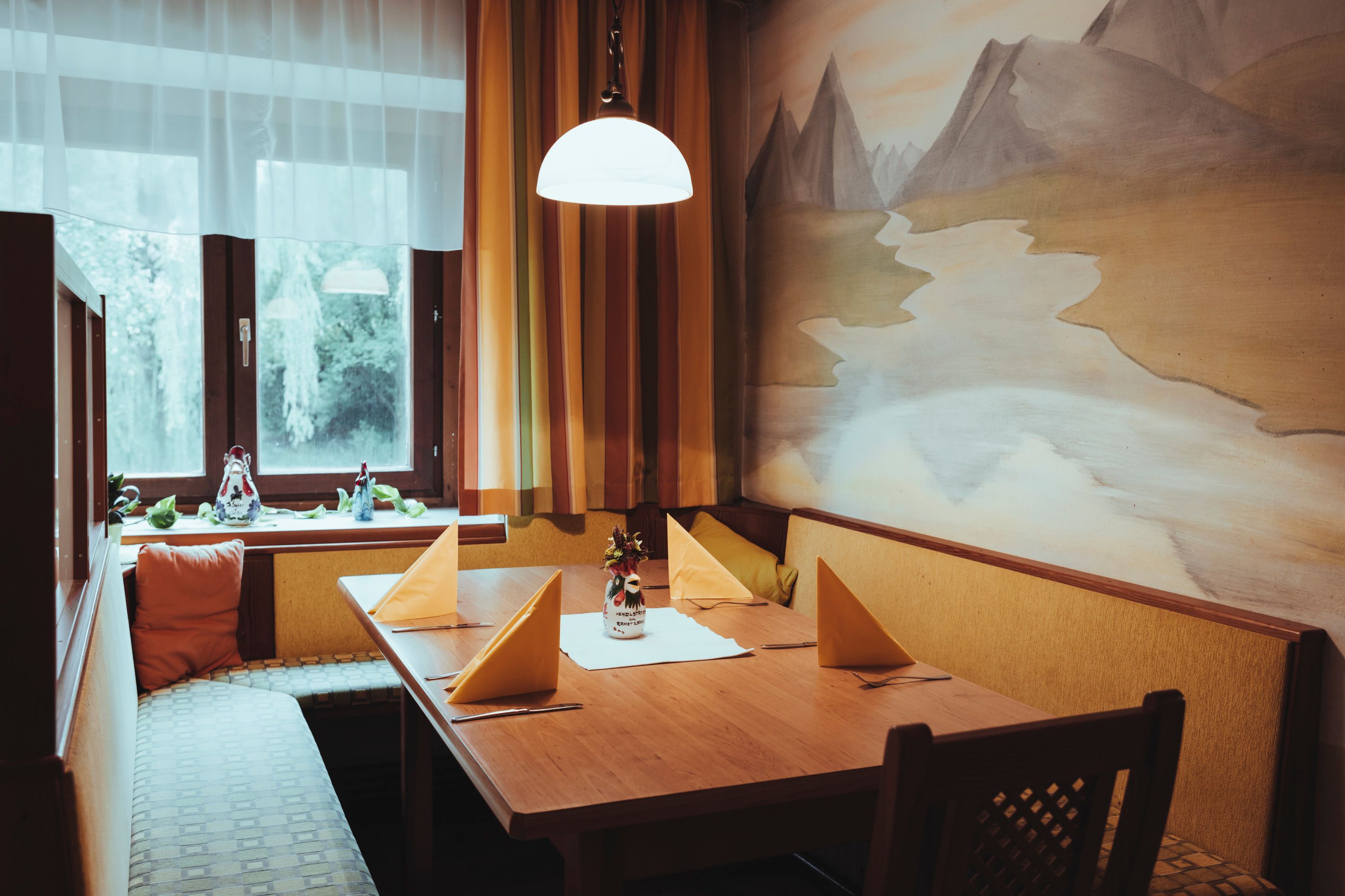 Útulné posezení s dřevěným stolem, žlutými ubrousky a nástěnnou malbou v restauraci.