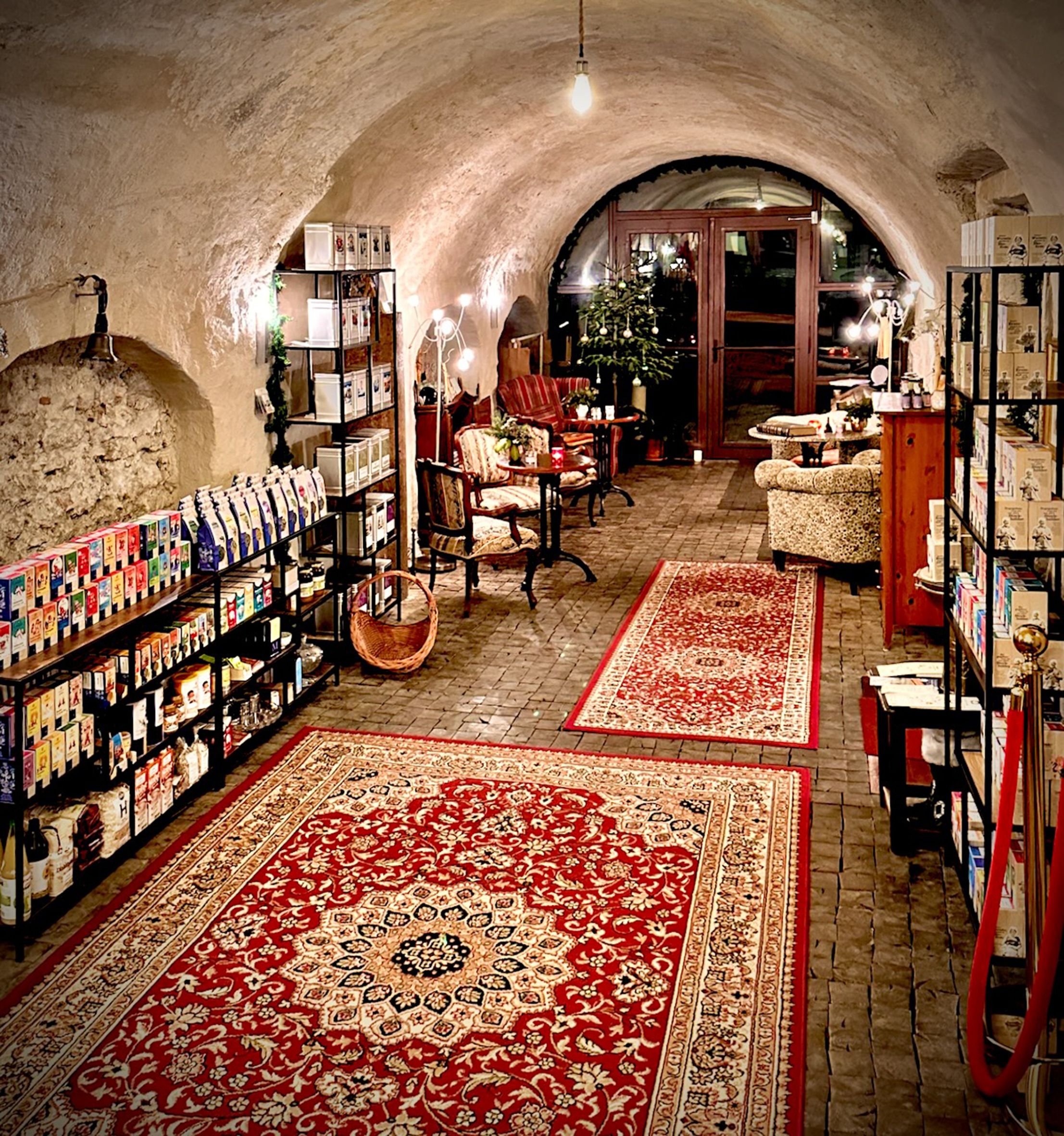 Útulná místnost s červenými koberci, policemi plnými výrobků a posezením v čajovně.