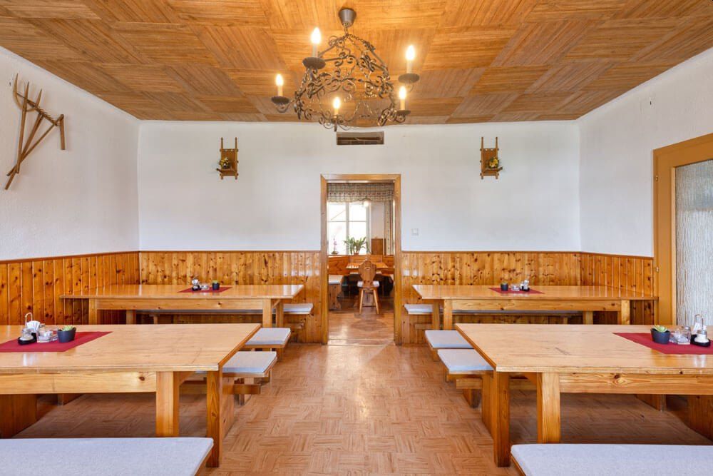 Pohled do interiéru tradiční vinárny s dřevěnými stoly a lavicemi, dřevěným obložením stěn a lustrem na stropě.