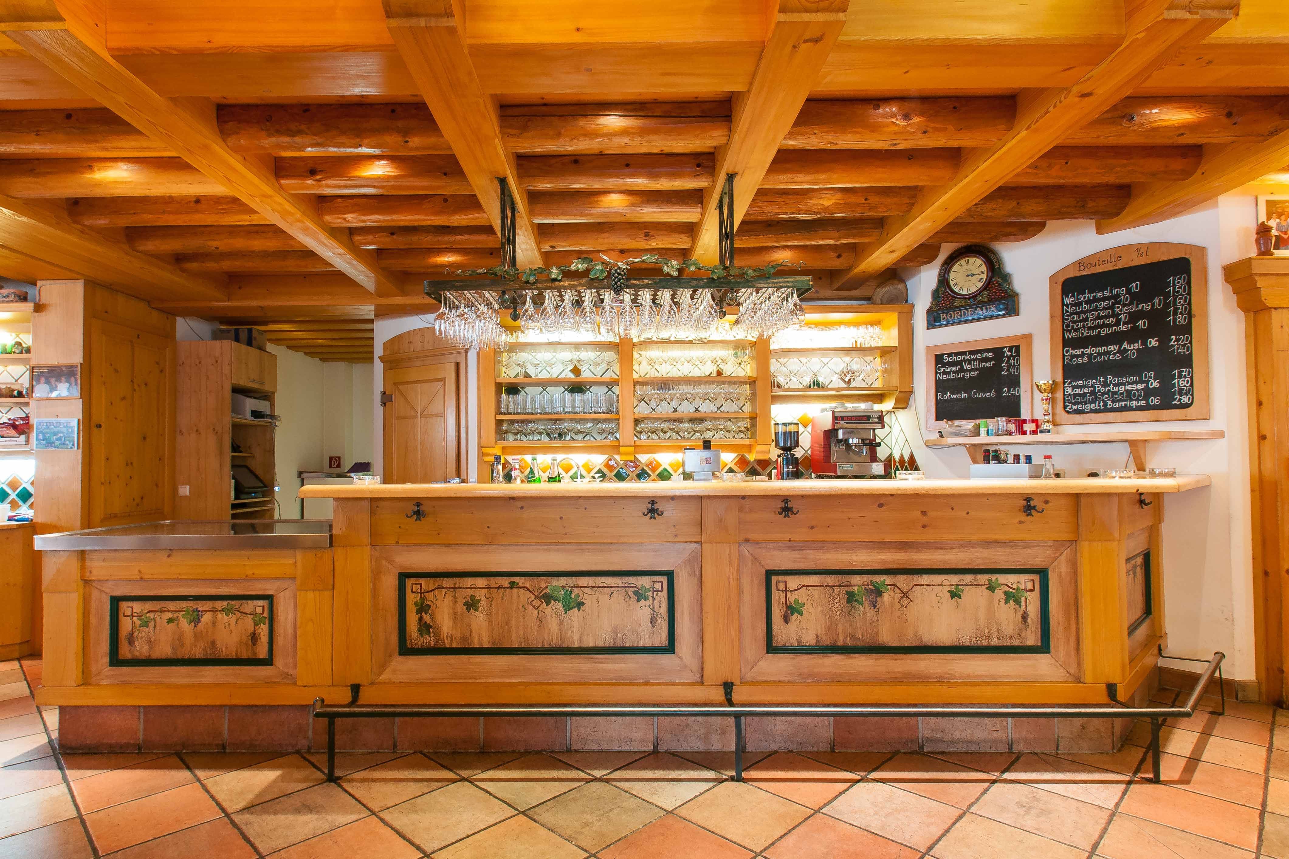 Rustikální bar s dřevěnými prvky a sklenicemi na víno na stropě.