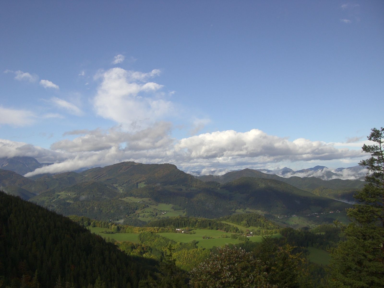 Panoramatický pohled na zelenou horskou krajinu pod modrou oblohou s mraky.