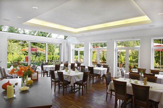 Pohled do interiéru světlé restaurace s velkými okny a prostřenými stoly.