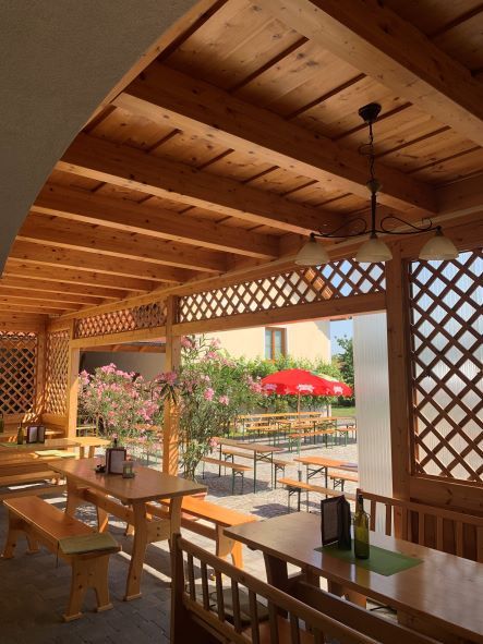 Dřevěná pergola se stoly a lavicemi, výhled do zahrady s červenými slunečníky.