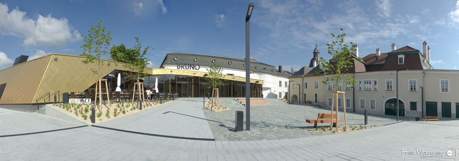 Moderní architektura se zlatou fasádou a tradiční budova v pozadí, modrá obloha.