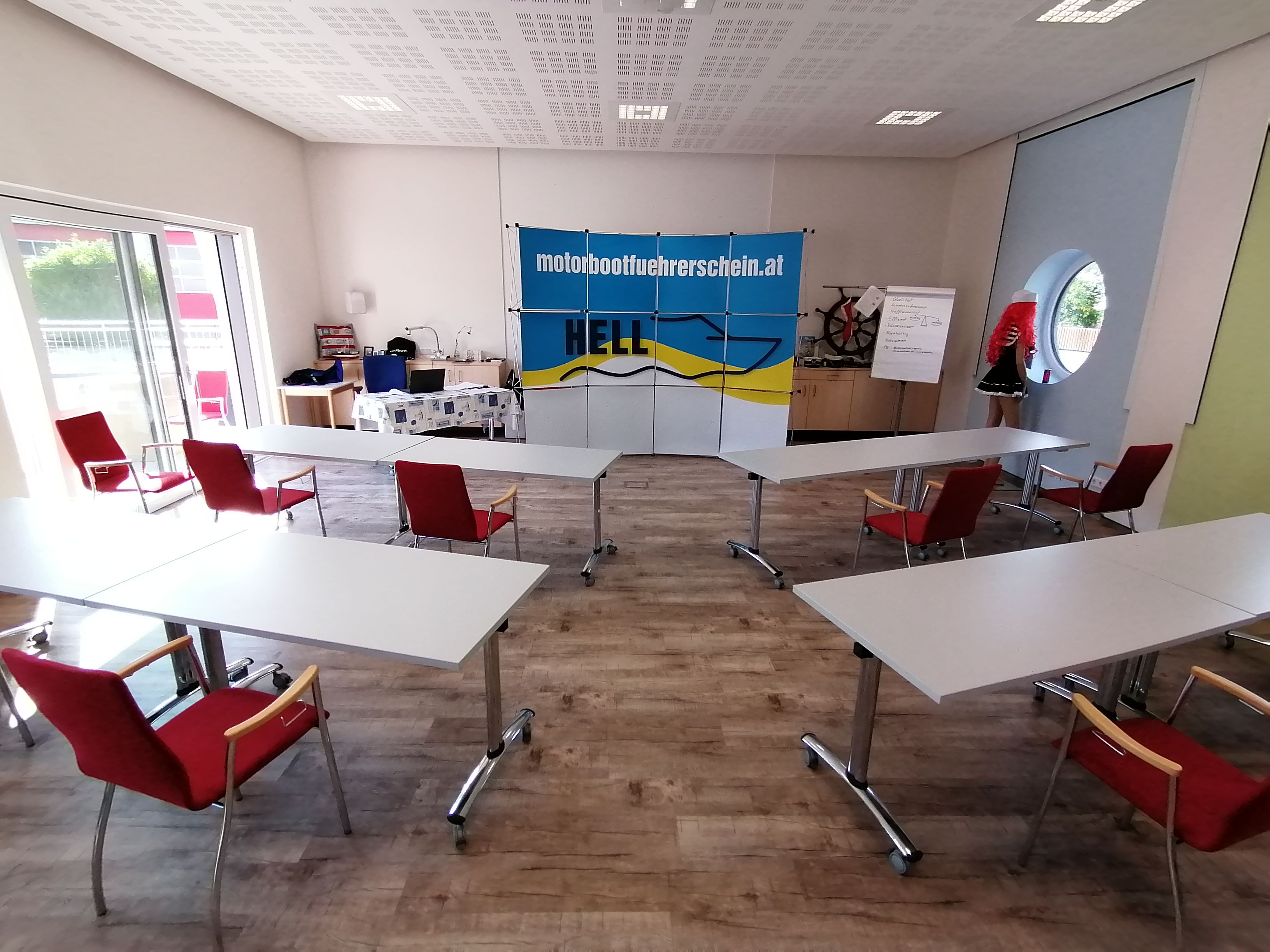 Školící místnost se stoly a židlemi, plakátem školy kapitána Pekla, flipchartem a figurínou.