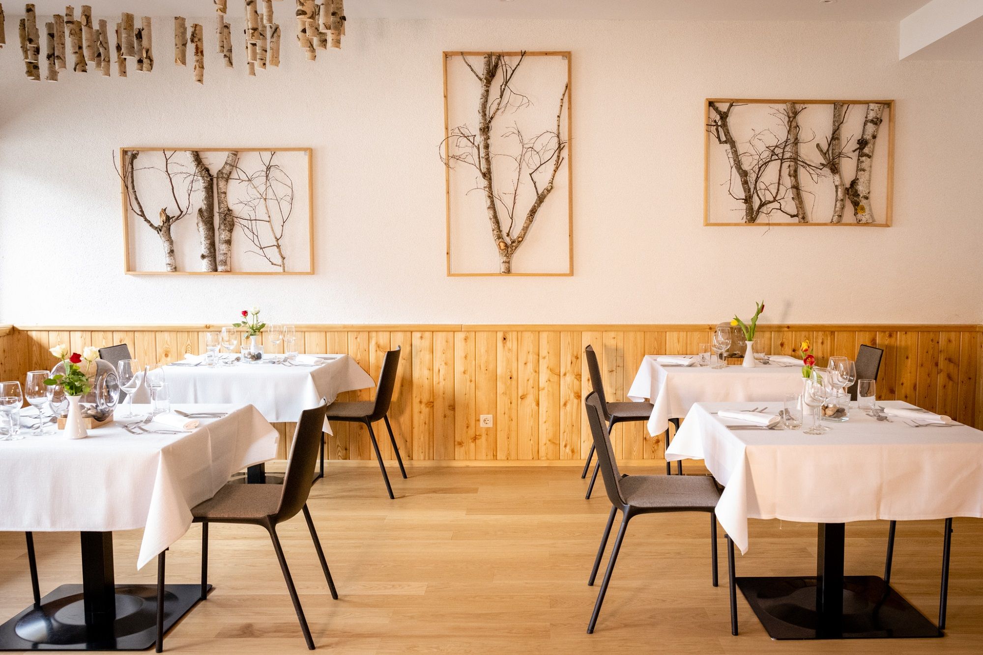 Elegantní restaurace s dřevěnými stěnami, bílými ubrusy a uměleckými díly z břízy na stěnách.