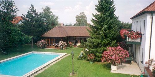 Udržovaná zahrada s bazénem, stromy a domkem s balkonem.